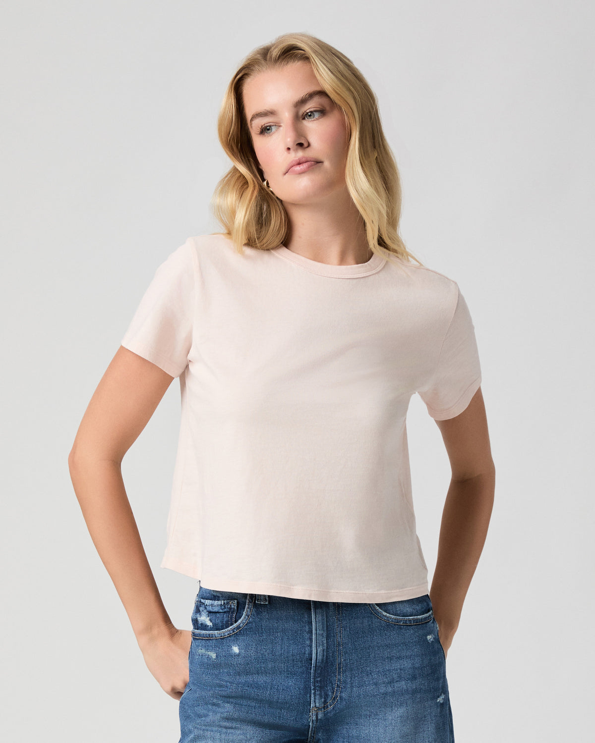 Rhodes Tee in Whisper Pink, a light pink crewneck tee; close-up of model facing forward with arms at her sides, worn with light blue jeans