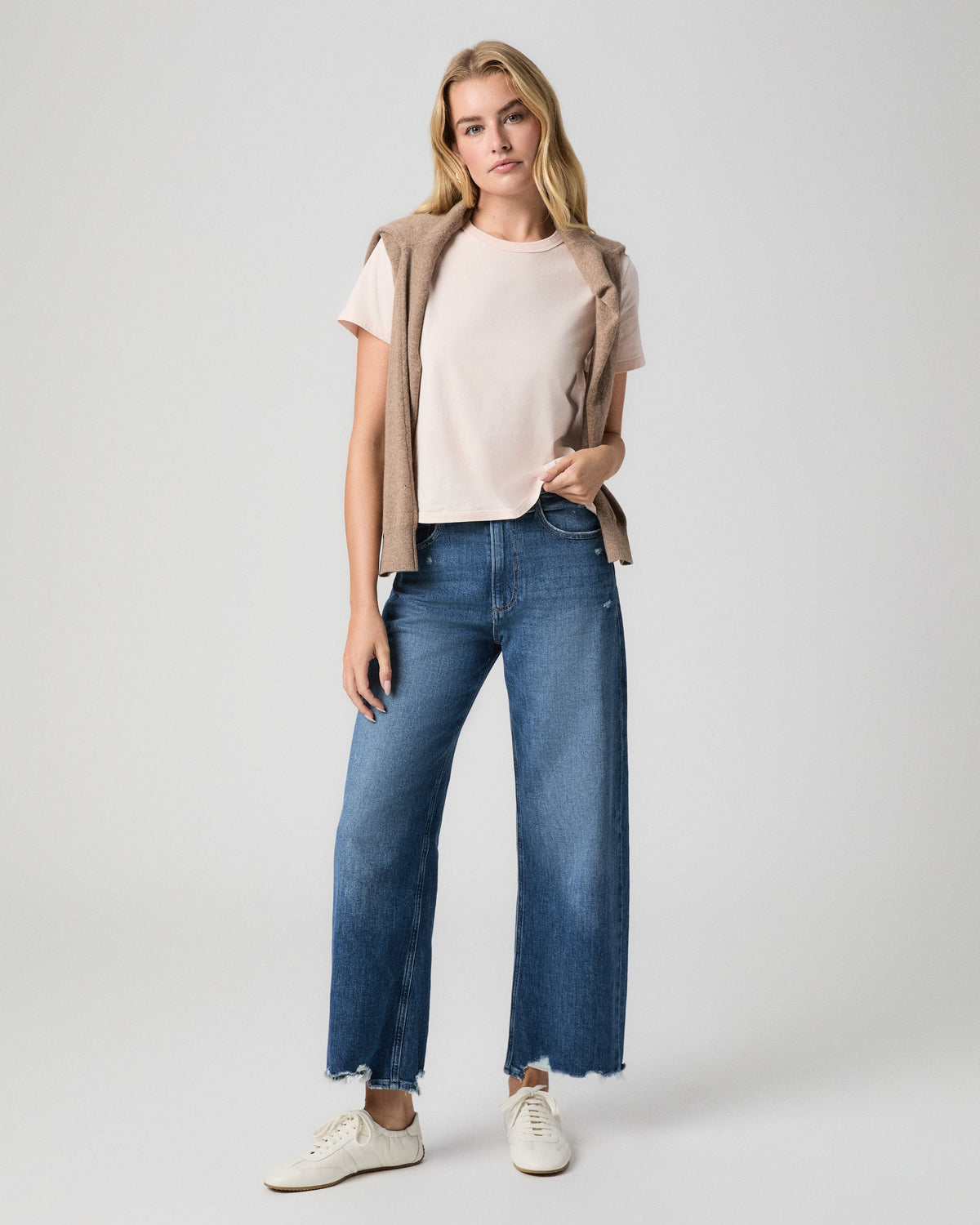 Rhodes Tee in Whisper Pink; model stands with a hand in her pocket and a beige sweater over her shoulders, with blue wide leg jeans and white sneakers