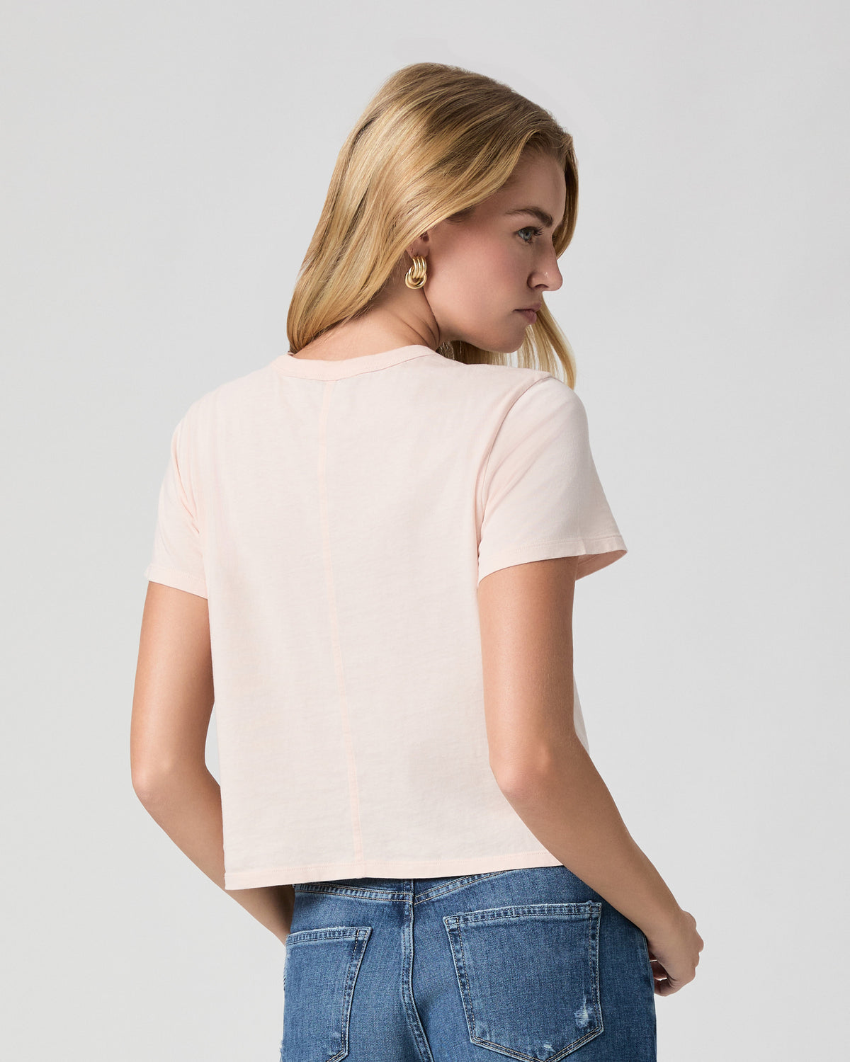 Back view of the Rhodes Tee in Whisper Pink; model looks over her shoulder, worn with light blue jeans