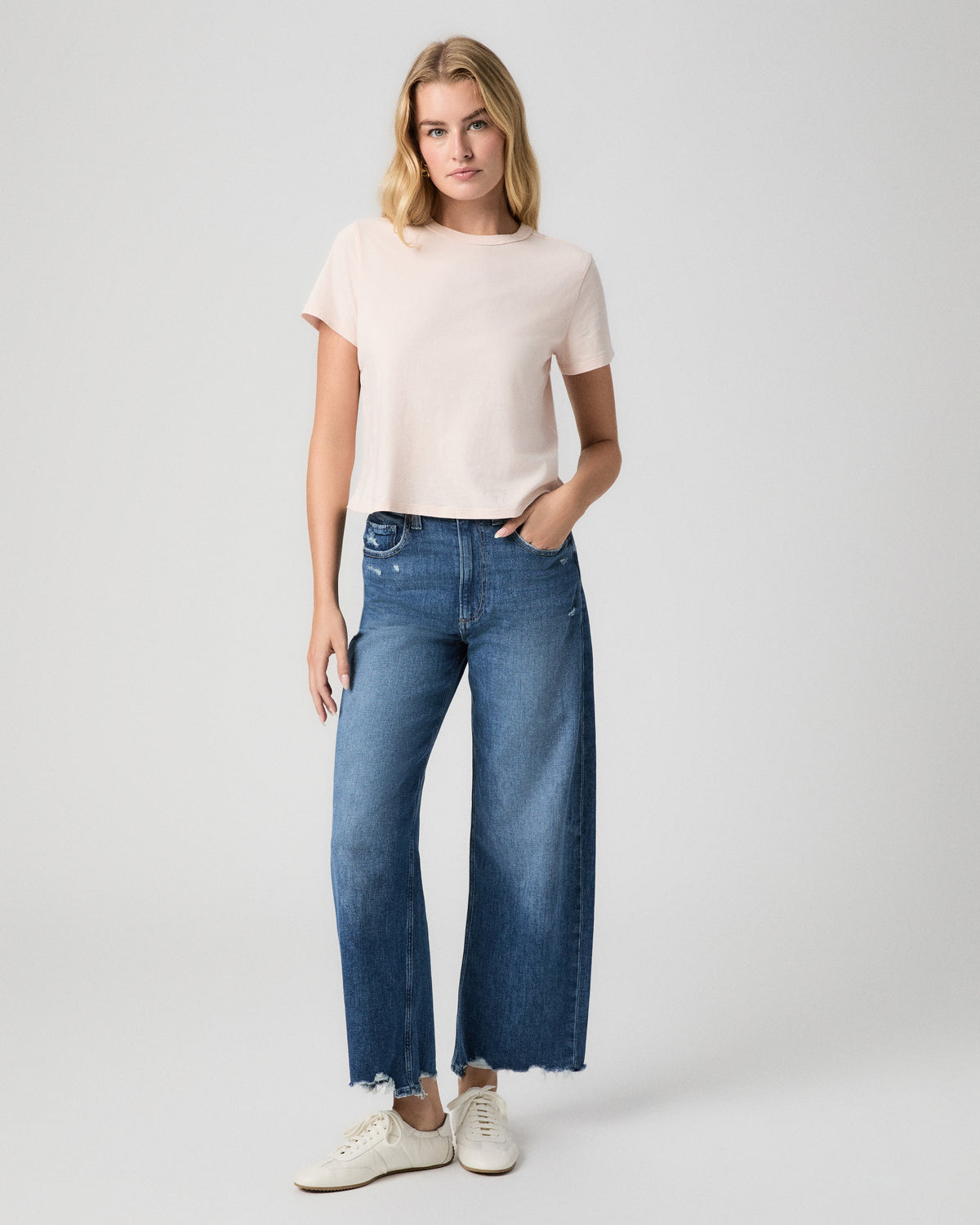Rhodes Tee in Whisper Pink; model stands facing forward with a hand in her pocket, in blue wide leg jeans and white sneakers