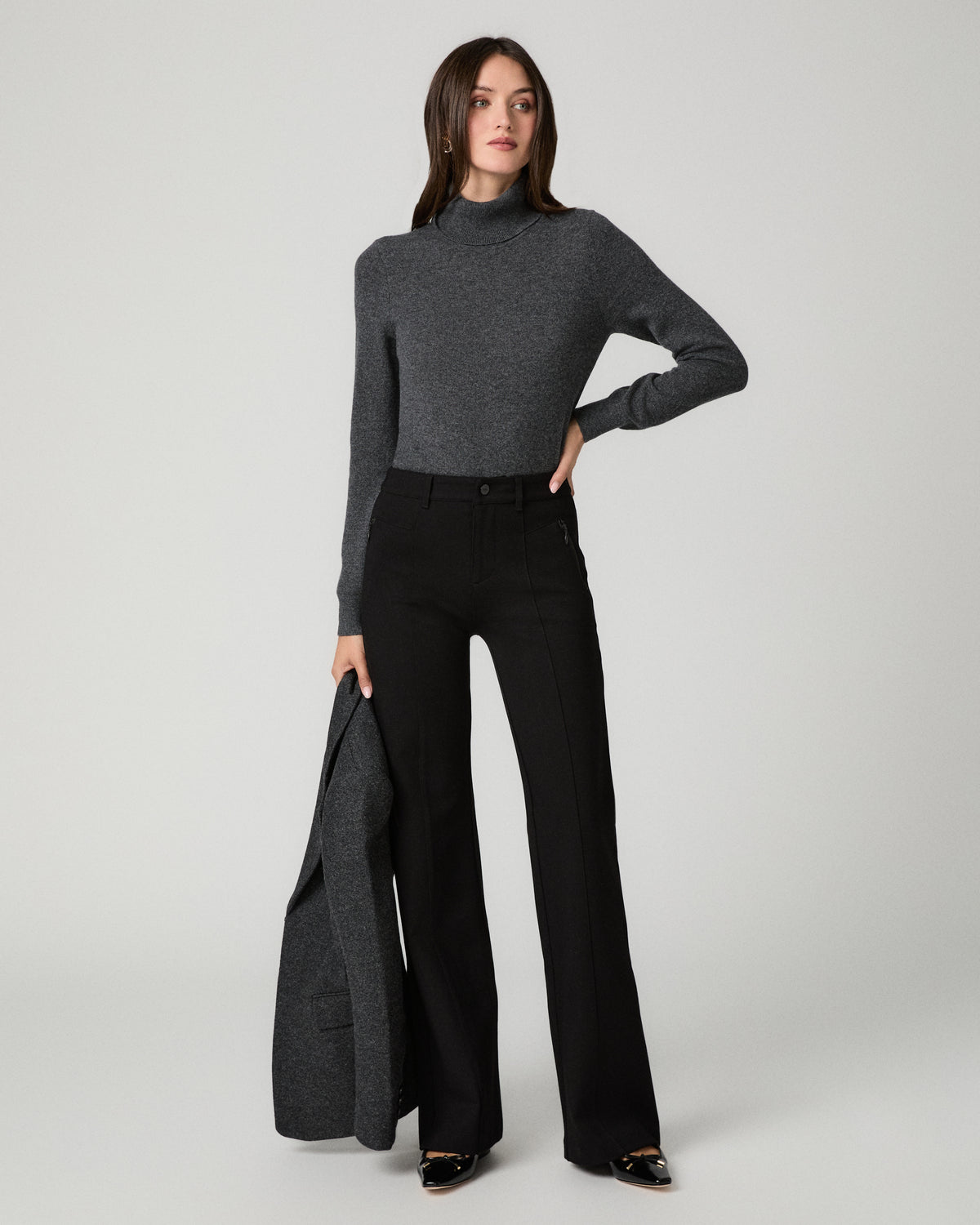 Women wearing a grey long sleeve top paired with black jeans and a grey blazer against a white background