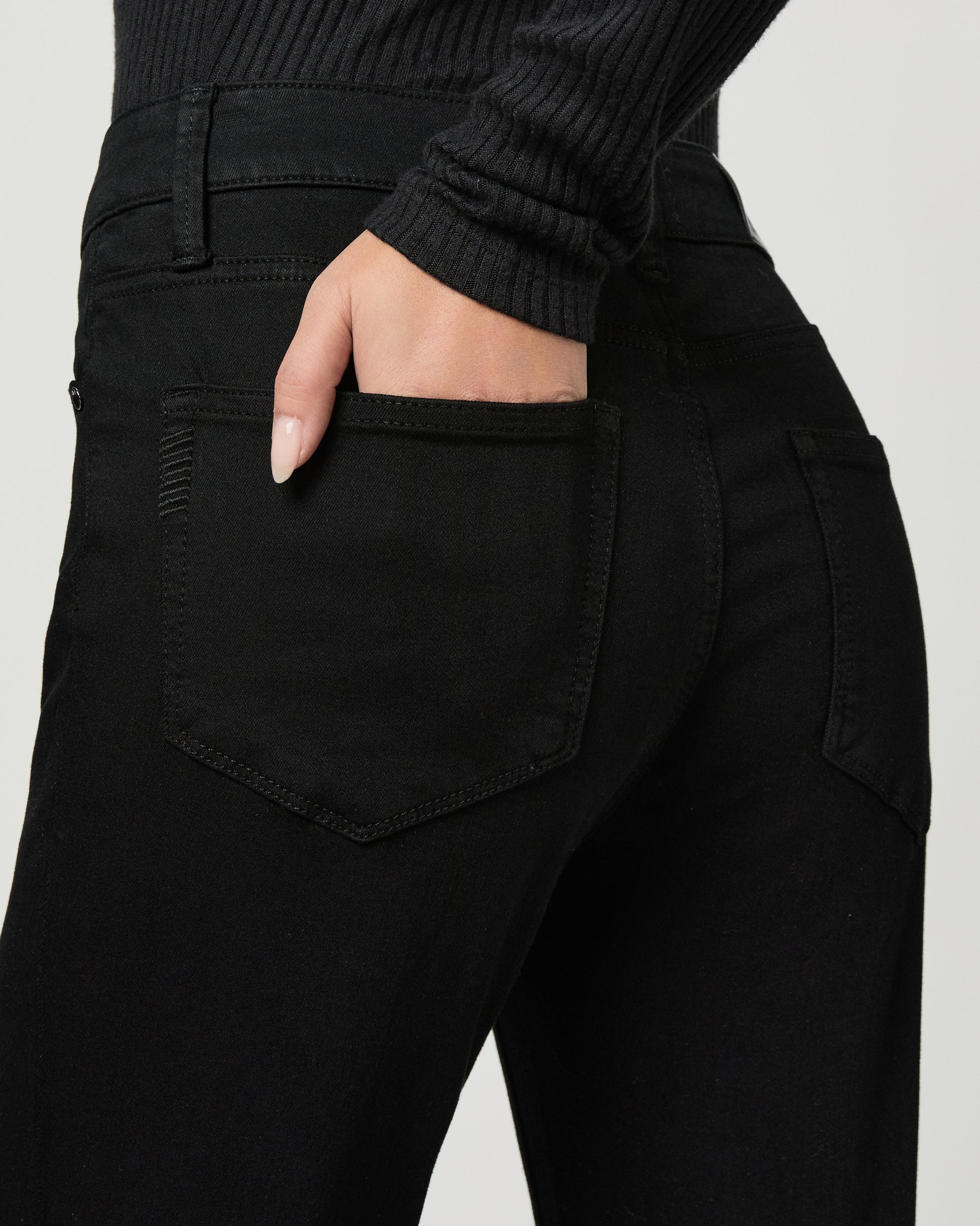 Woman wearing a black top and back jeans on a white background