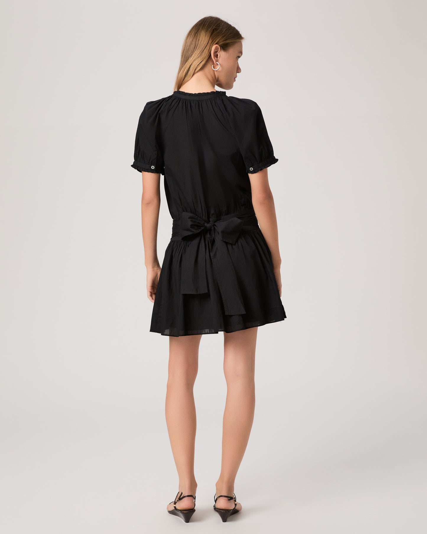 Model wearing a black dress paired with dark brown sandals against a white background. 