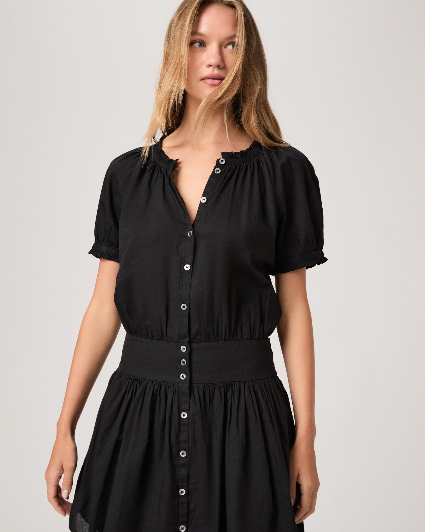 Model wearing a black dress paired with dark brown sandals against a white background. 