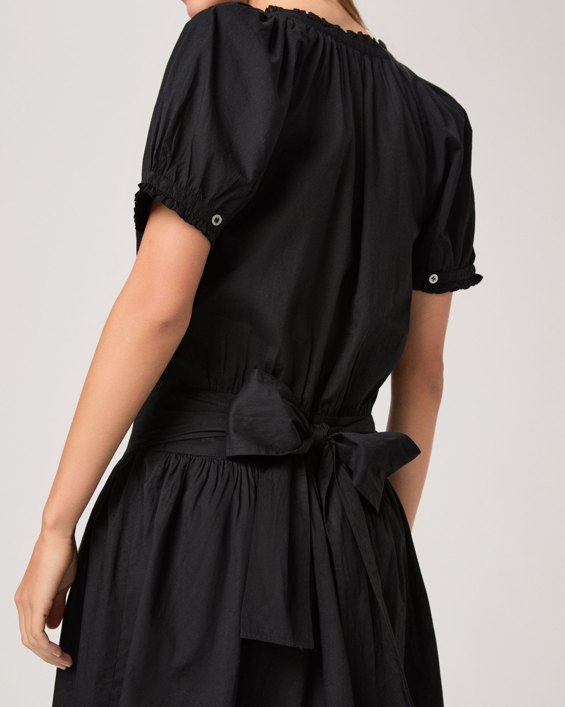 Model wearing a black dress paired with dark brown sandals against a white background. 