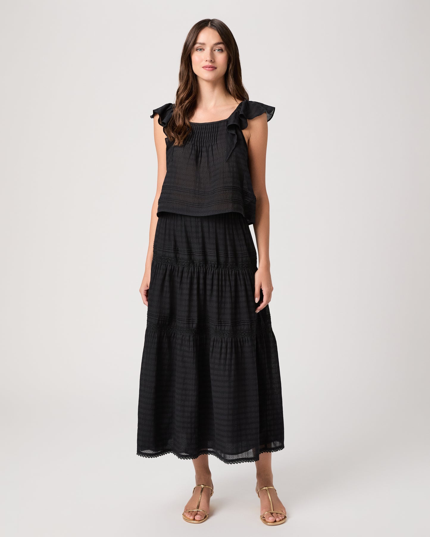 Model wearing a black midi skirt paired with a black  top and gold sandals