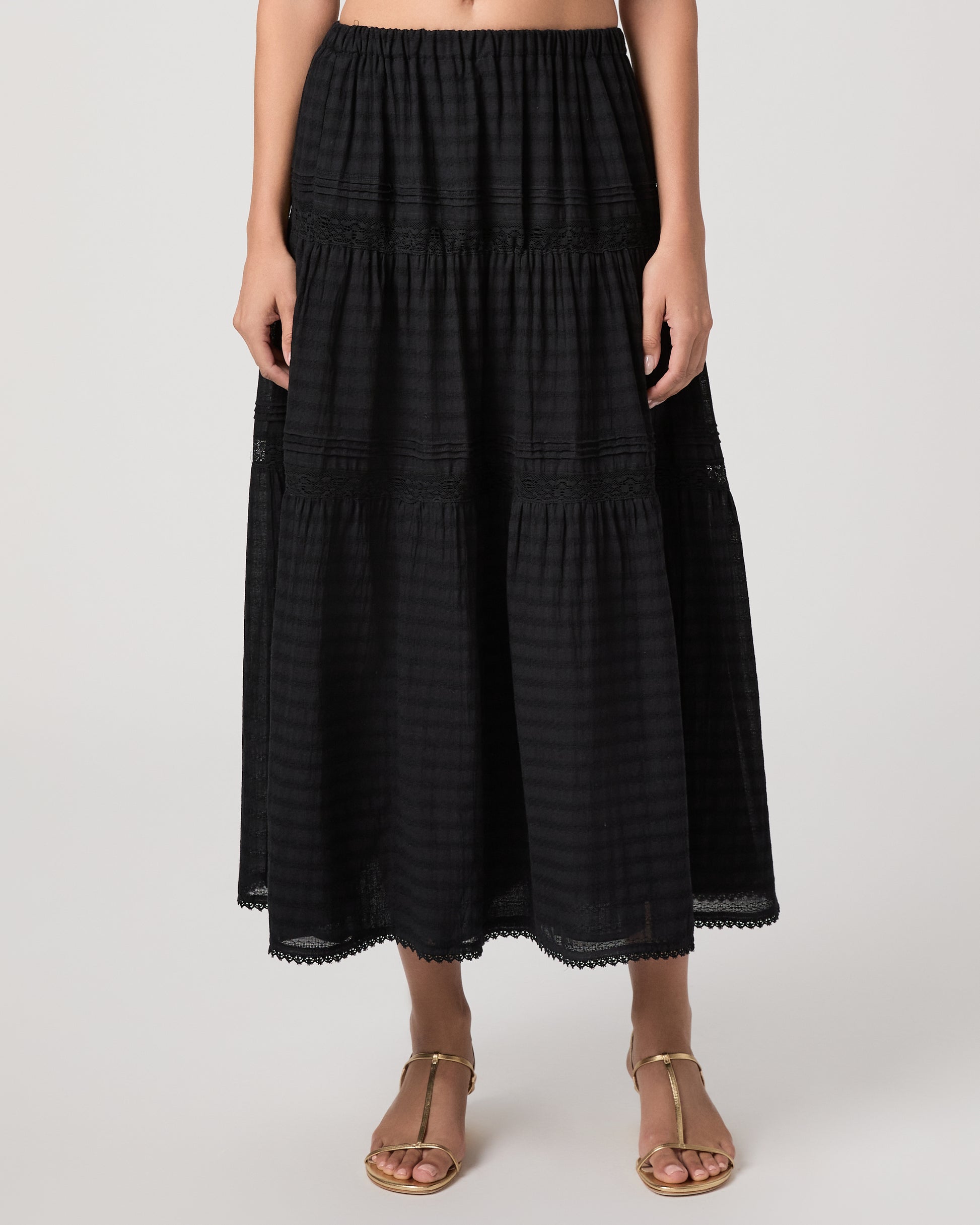Model wearing a black midi skirt paired with a black  top and gold sandals
