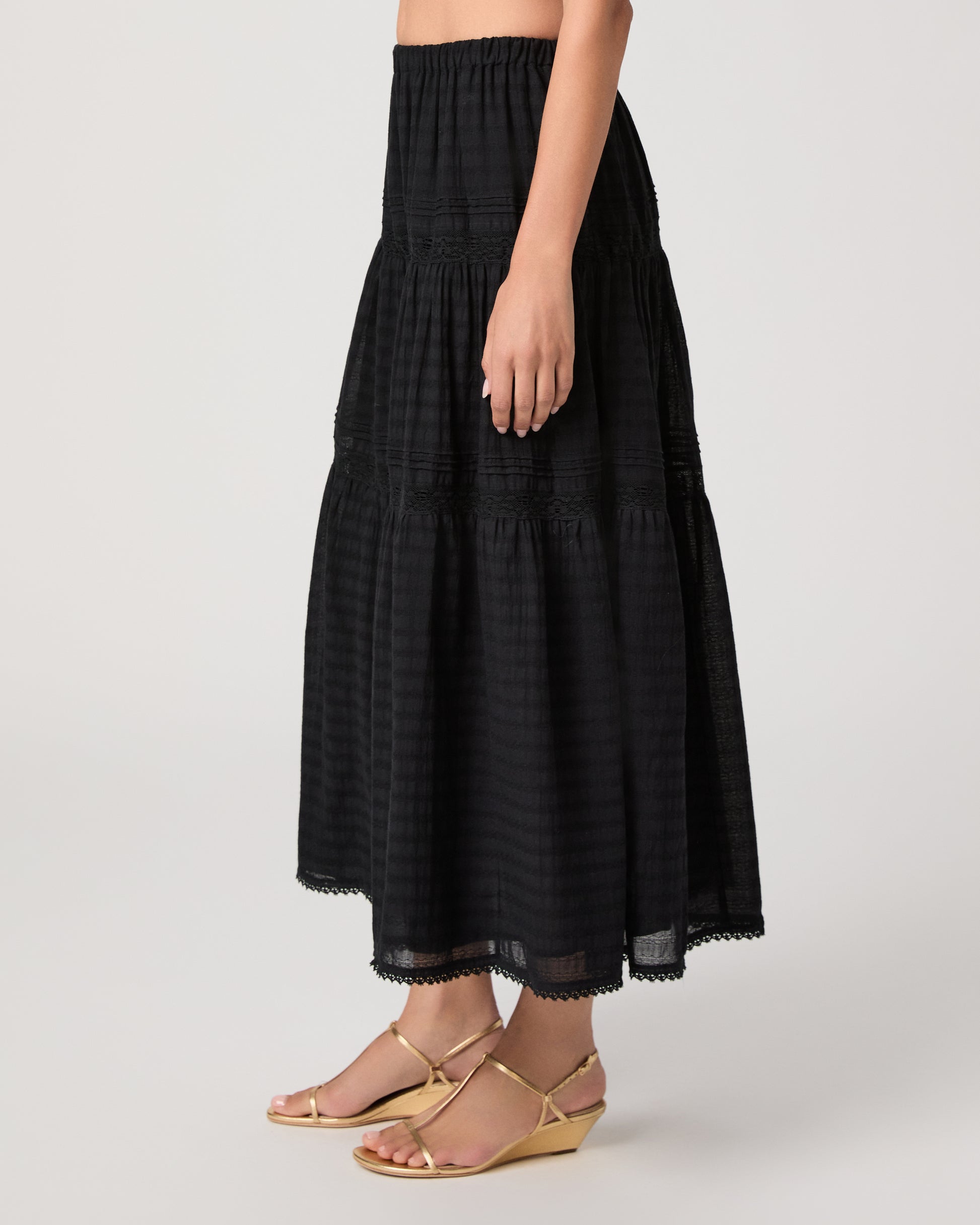 Model wearing a black midi skirt paired with a black  top and gold sandals