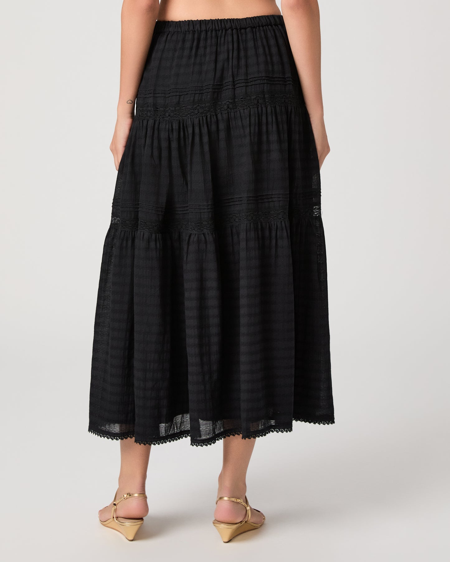Model wearing a black midi skirt paired with a black  top and gold sandals
