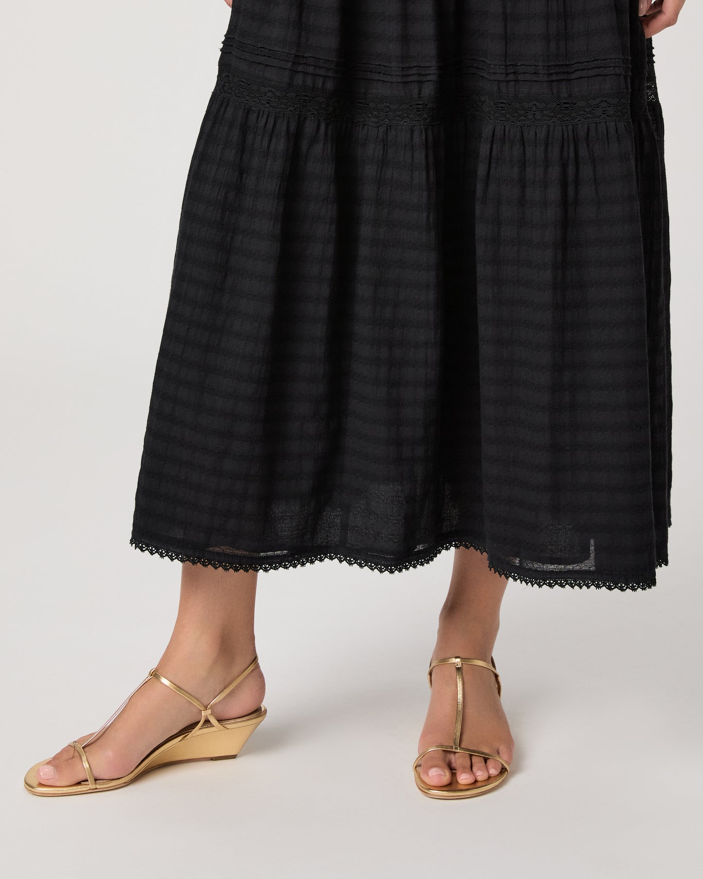 Model wearing a black midi skirt paired with a black  top and gold sandals