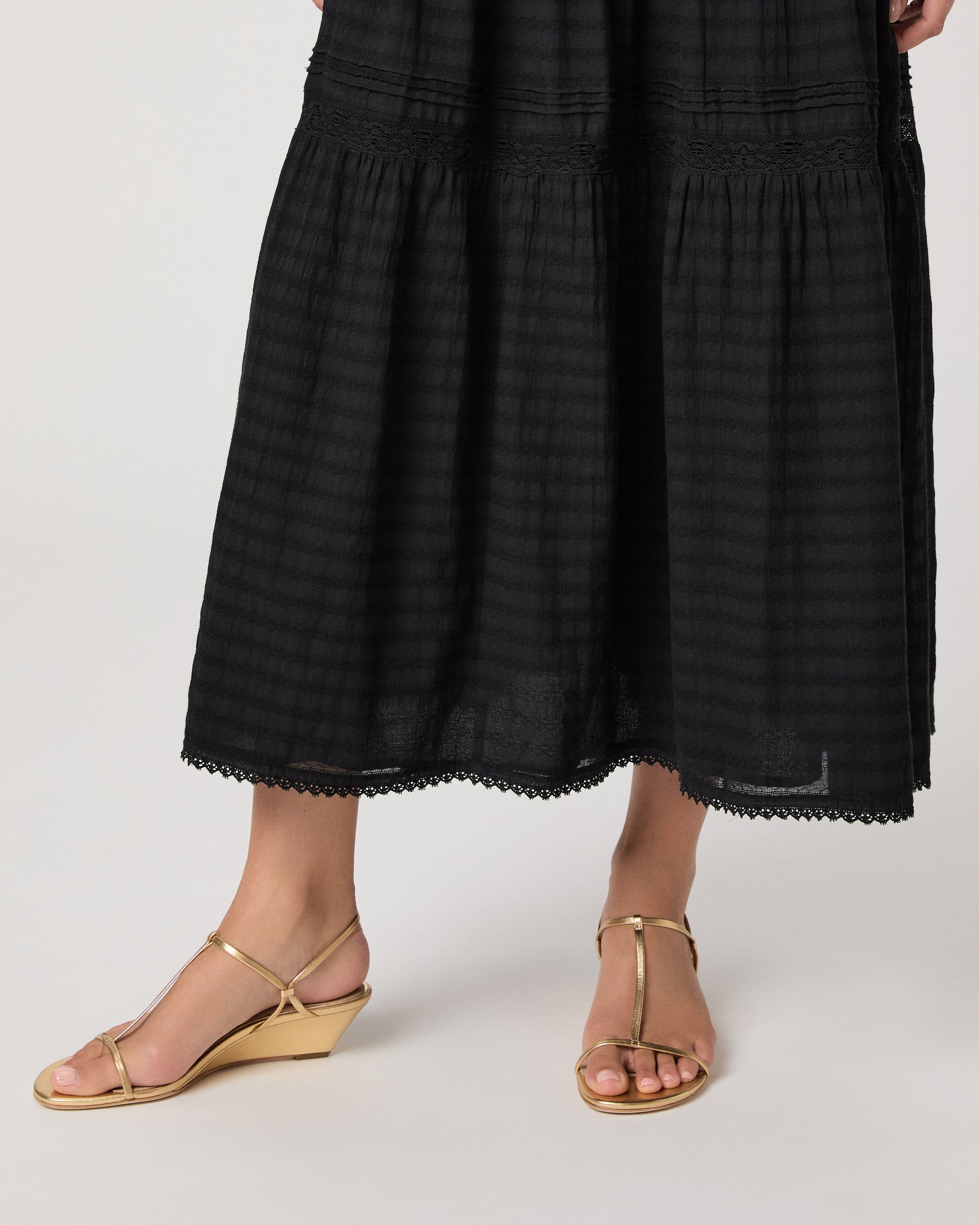 Model wearing a black midi skirt paired with a black  top and gold sandals