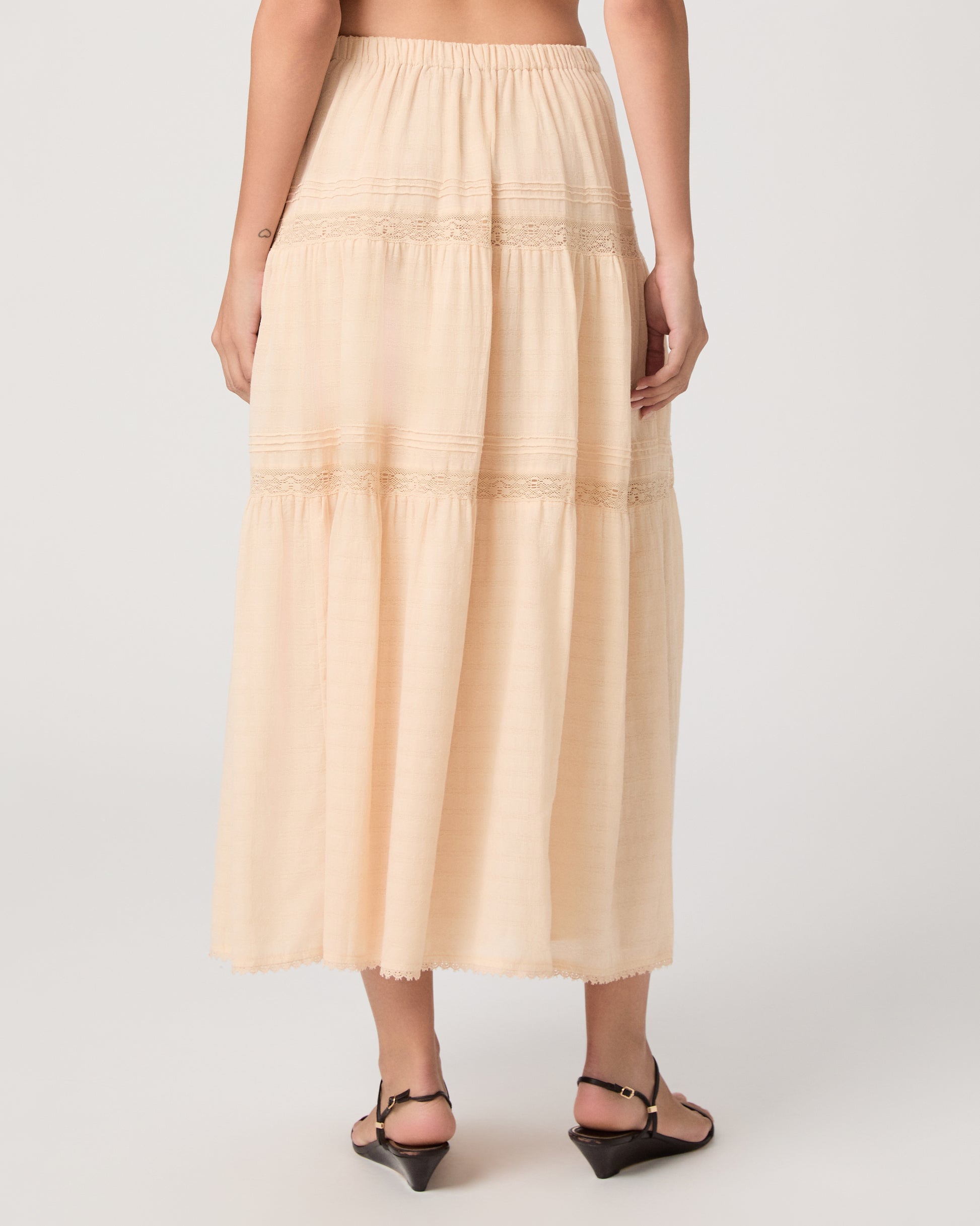 Model wearing a light peach midi skirt paired with a light peach top and brown sandals