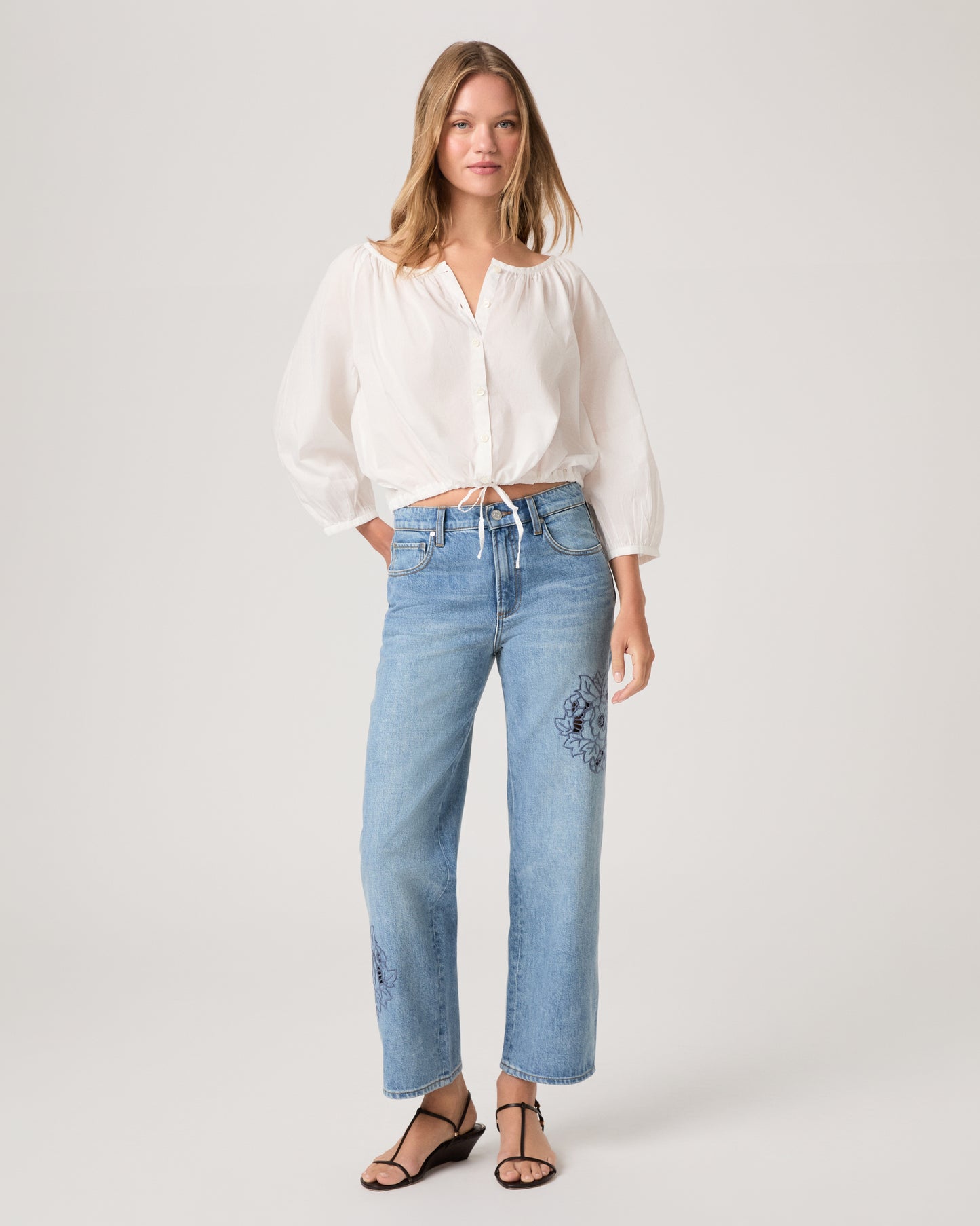 Women wearing a white blouse paired with light wash jeans against a white background.