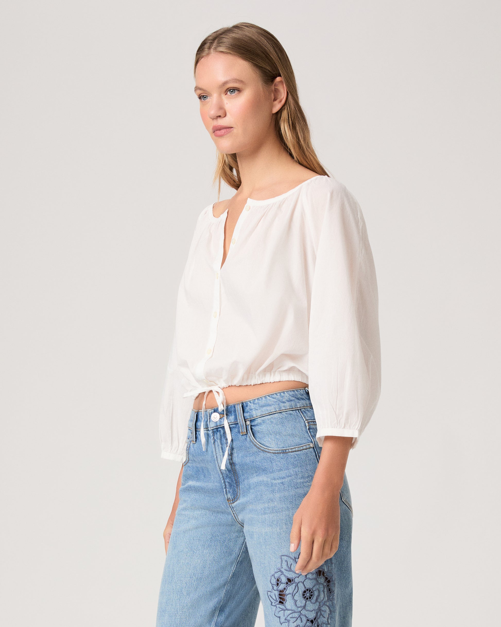 Women wearing a white blouse paired with light wash jeans against a white background.