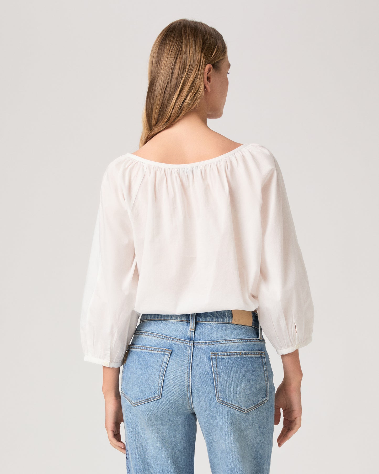Women wearing a white blouse paired with light wash jeans against a white background.