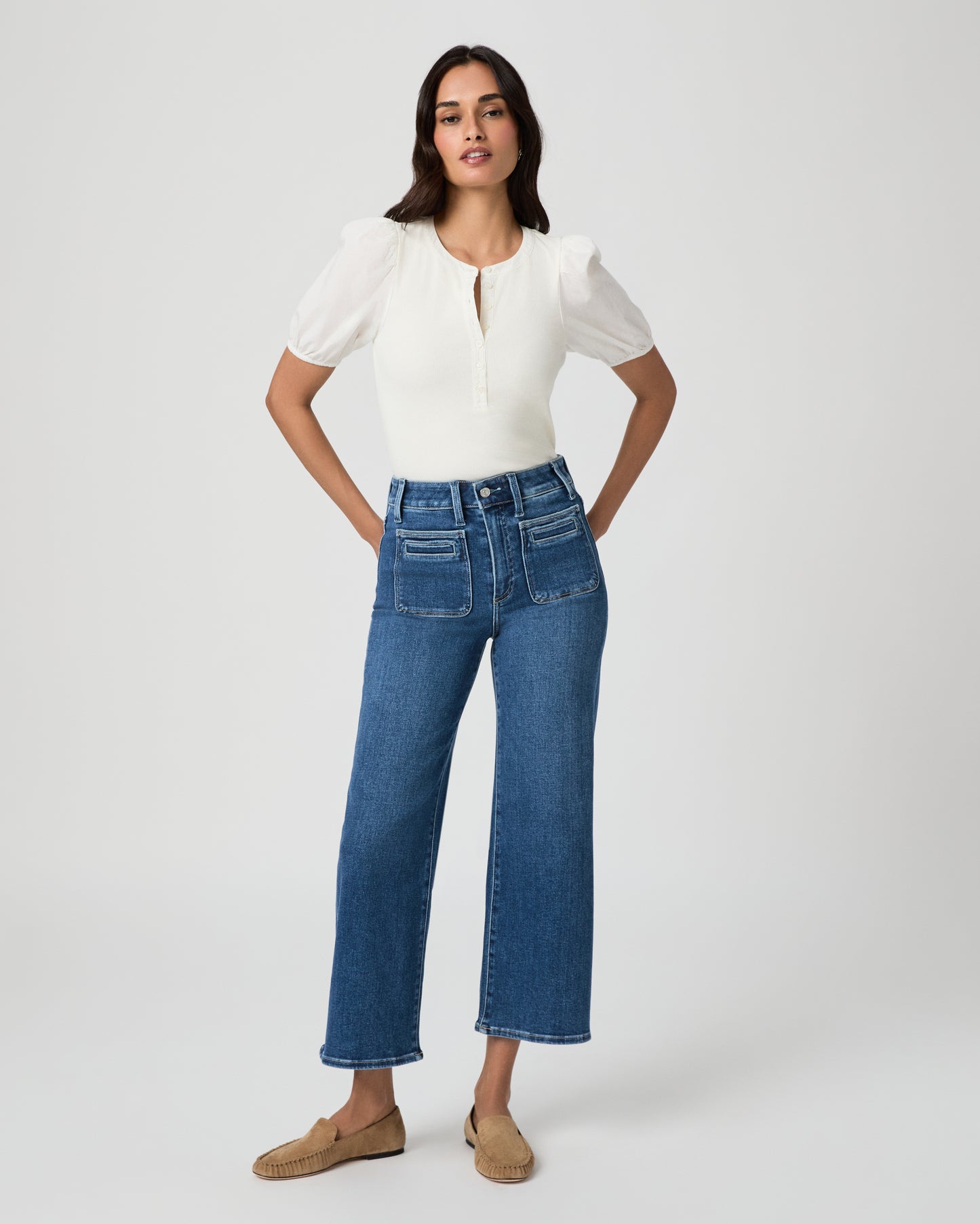 Woman wearing a white blouse and blue jeans paired with brown flats on a white background