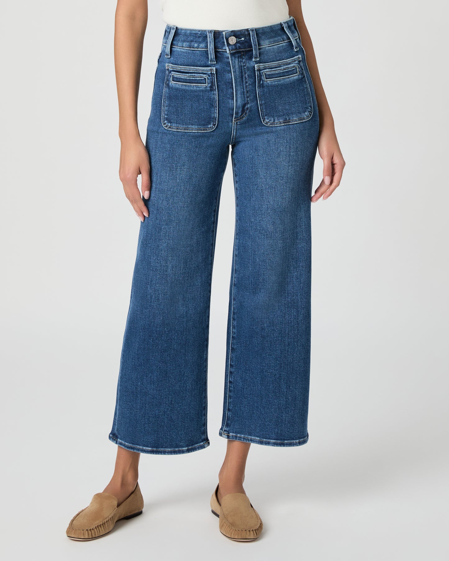 Woman wearing a white blouse and blue jeans paired with brown flats on a white background