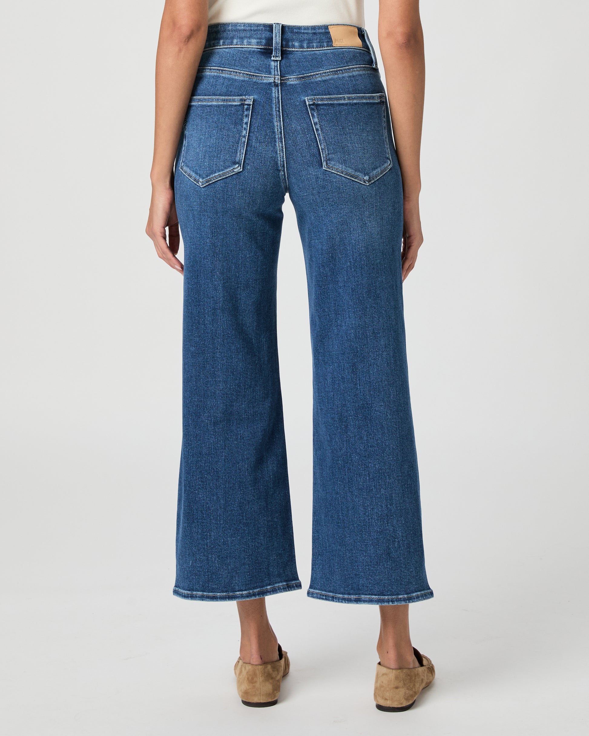 Woman wearing a white blouse and blue jeans paired with brown flats on a white background
