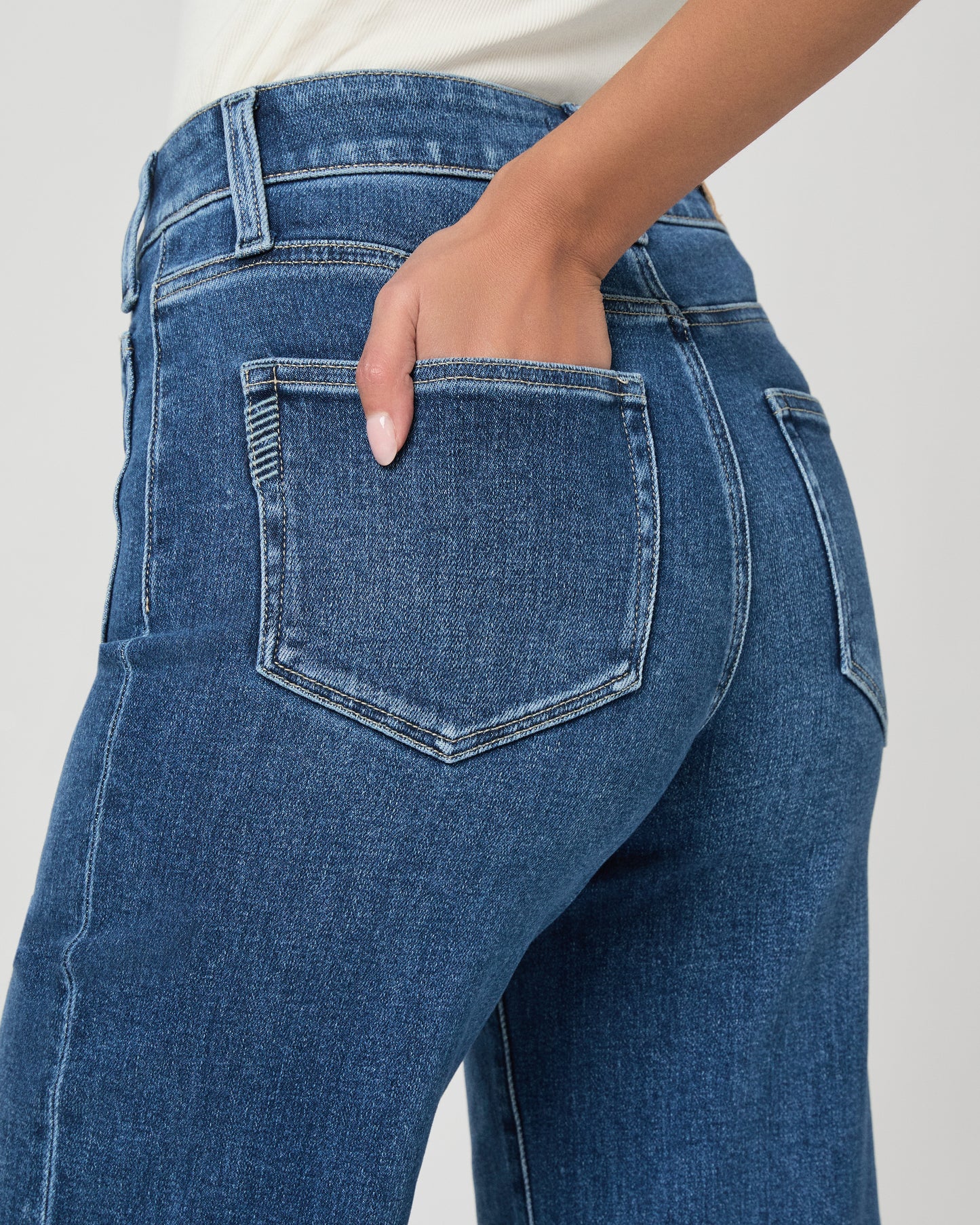 Woman wearing a white blouse and blue jeans paired with brown flats on a white background
