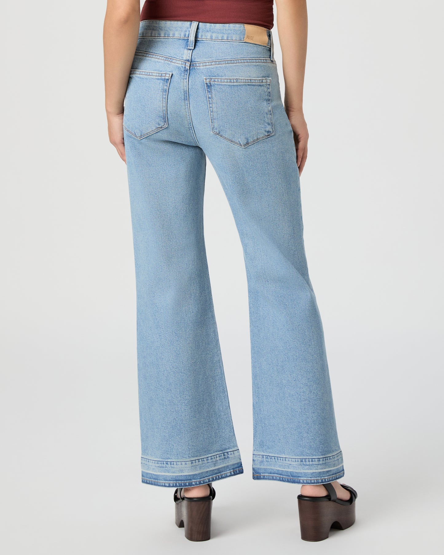 Woman wearing a sleeveless burgundy top and light blue jeans paired with black wedges on a white background