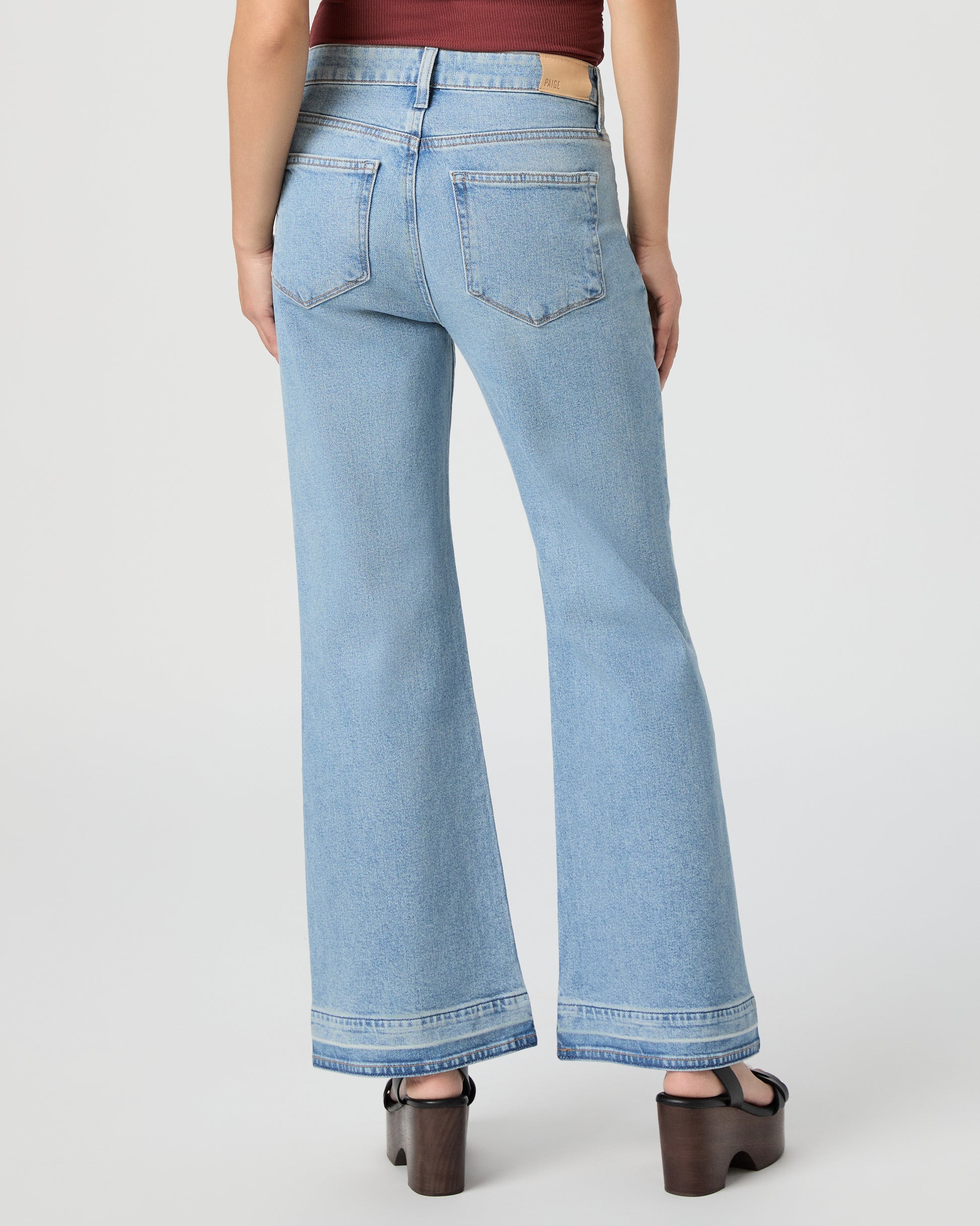Woman wearing a sleeveless burgundy top and light blue jeans paired with black wedges on a white background