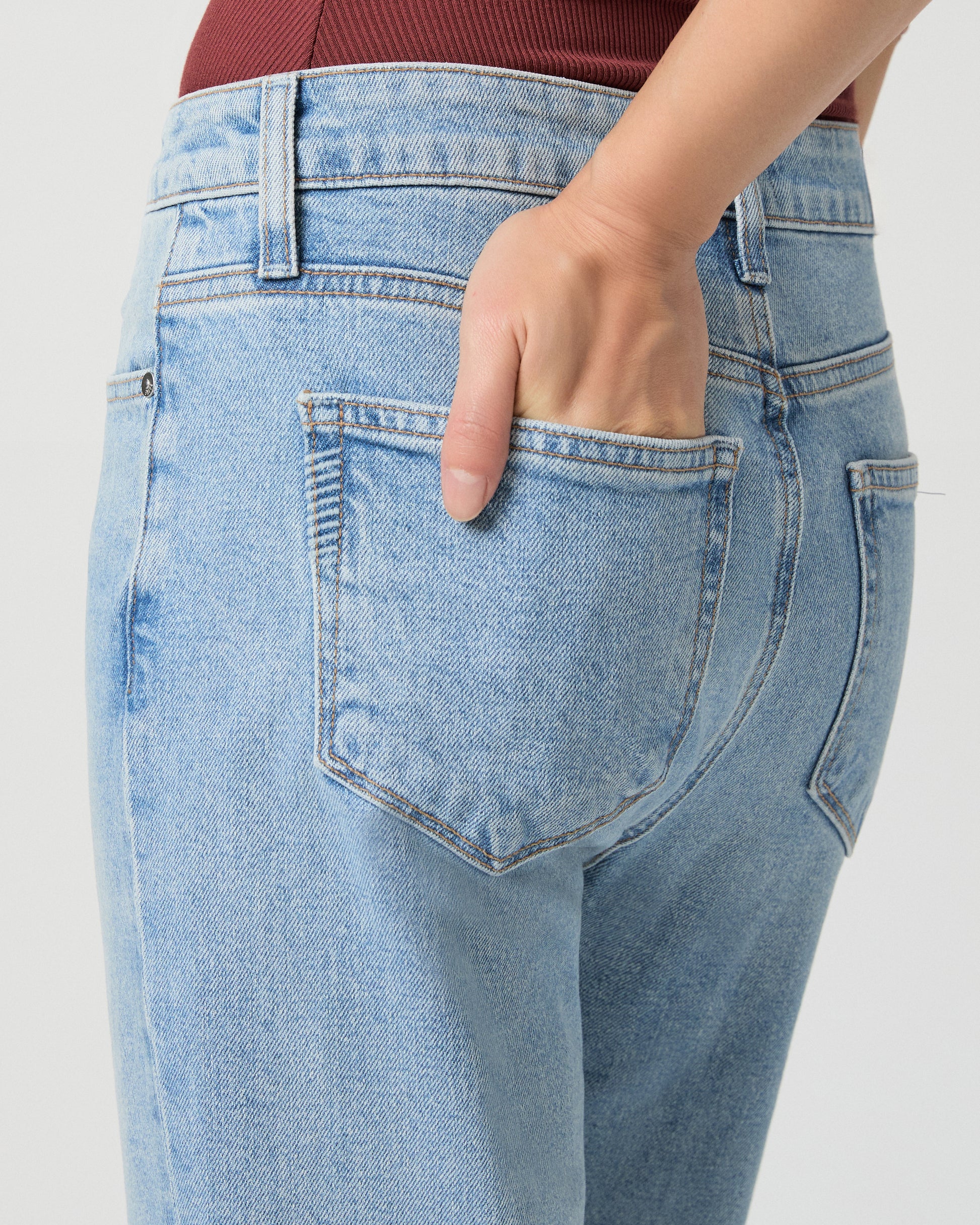 Woman wearing a sleeveless burgundy top and light blue jeans on a white background