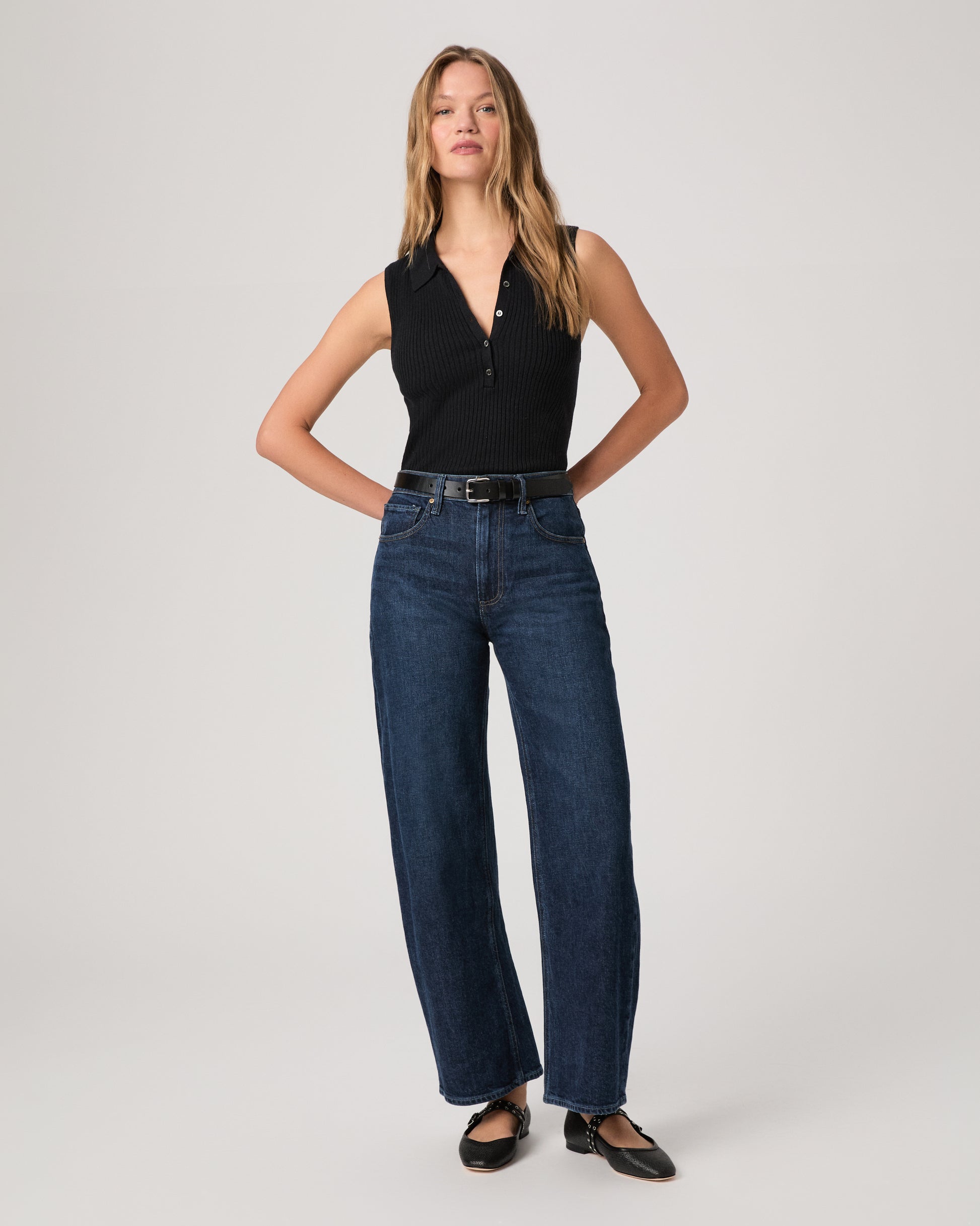 Women wearing a black top paired with dark wash denim and black flats against a white background 
