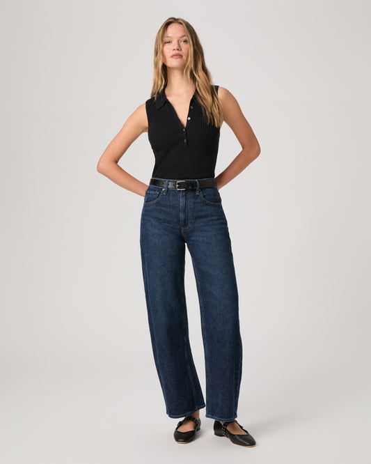 Women wearing a black top paired with dark wash denim and black flats against a white background 