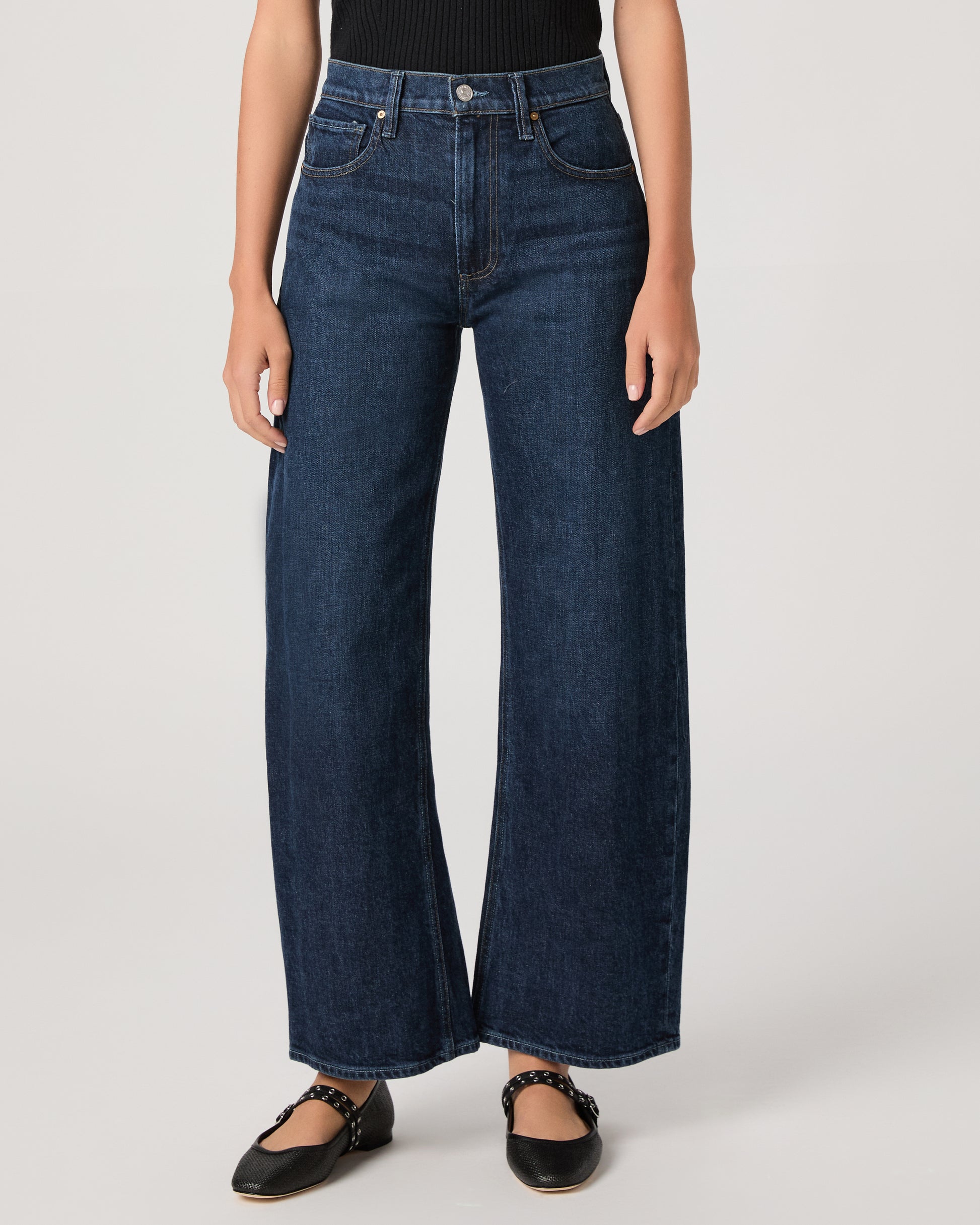 Women wearing a black top paired with dark wash denim and black flats against a white background 