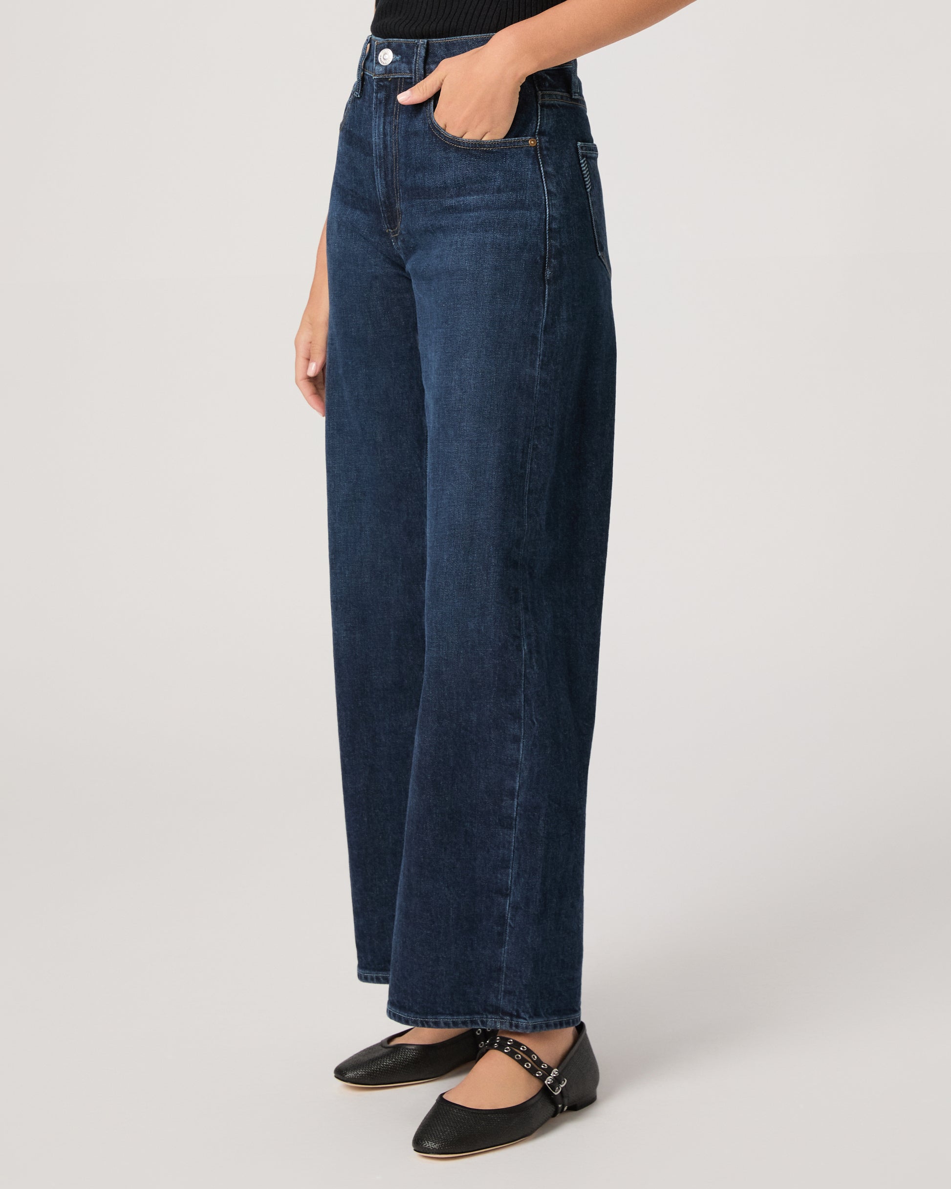 Women wearing a black top paired with dark wash denim and black flats against a white background 