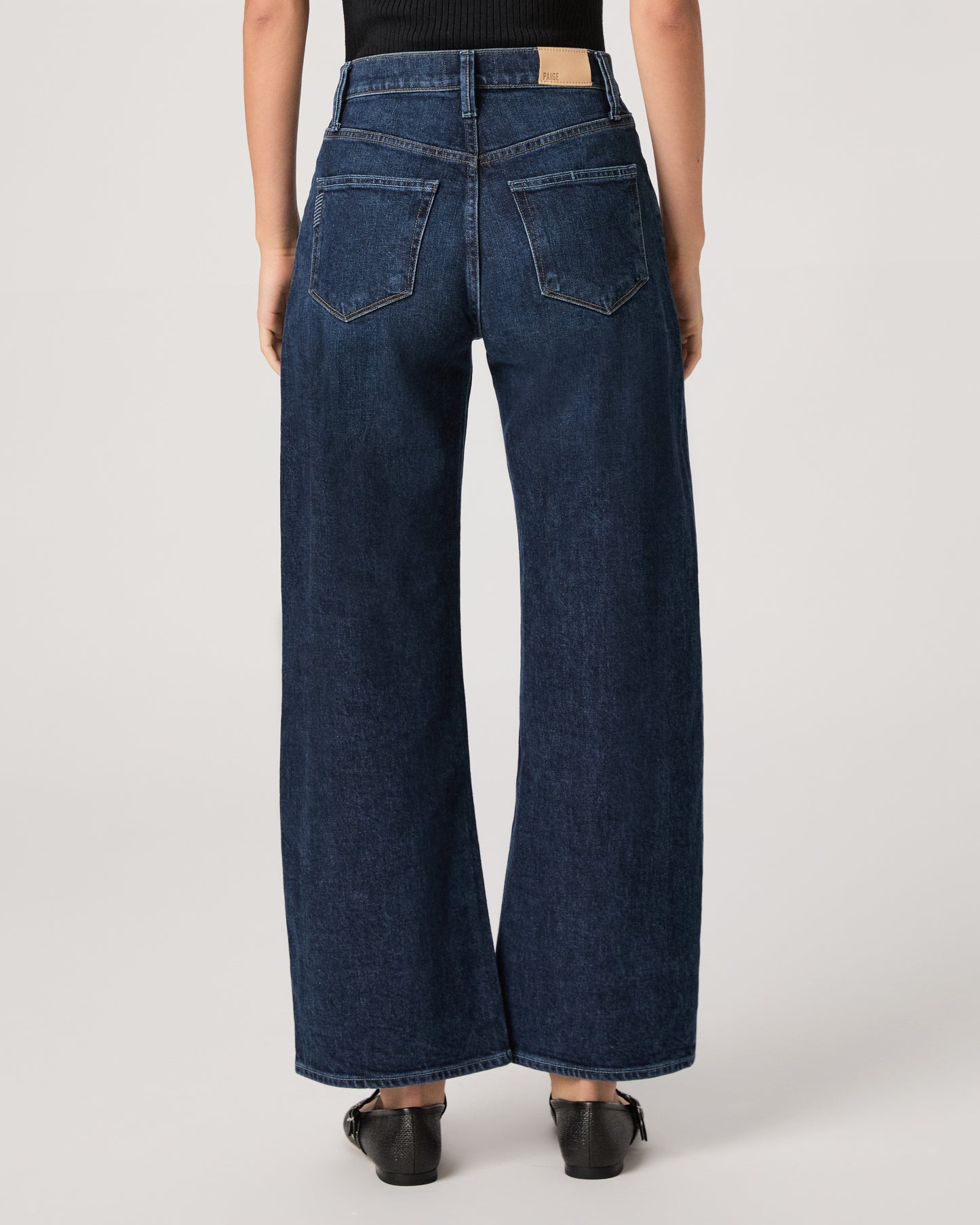 Women wearing a black top paired with dark wash denim and black flats against a white background 