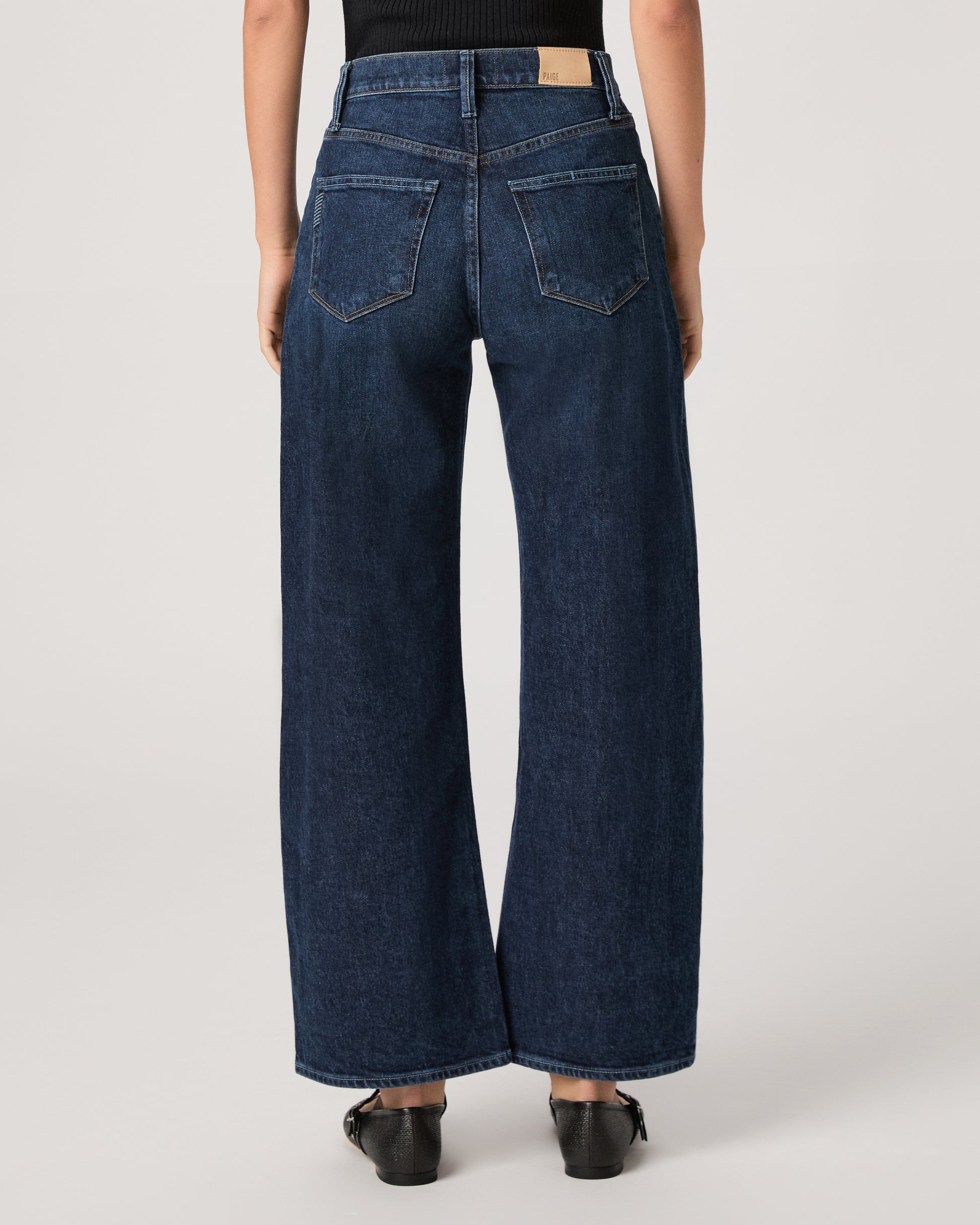 Women wearing a black top paired with dark wash denim and black flats against a white background 