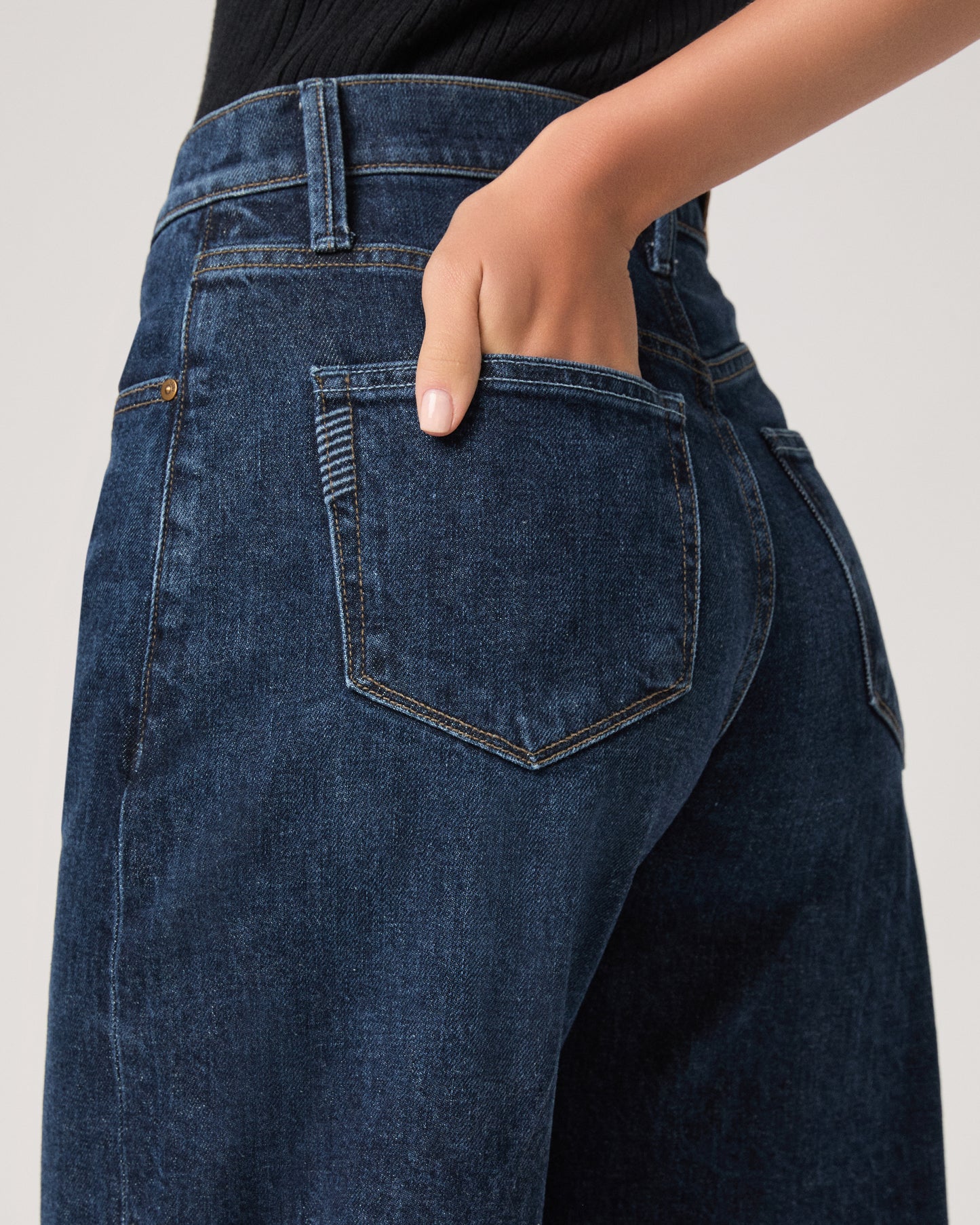 Women wearing a black top paired with dark wash denim and black flats against a white background 
