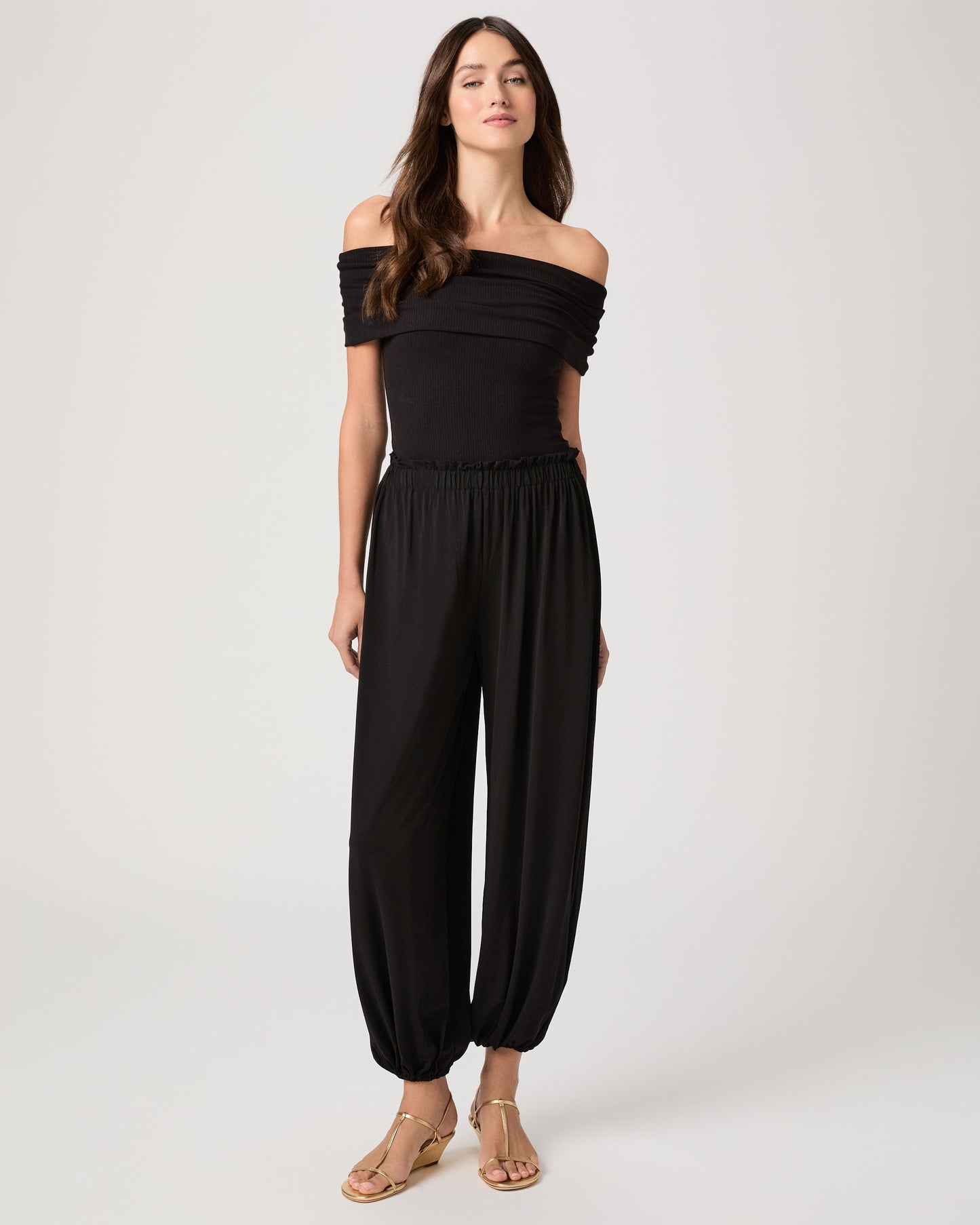 Model wearing a black pant paired with a black off the shoulder top and gold sandals