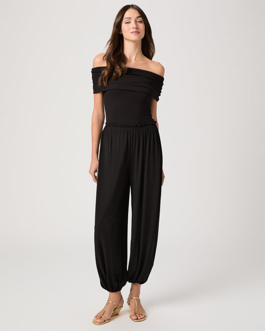 Model wearing a black pant paired with a black off the shoulder top and gold sandals