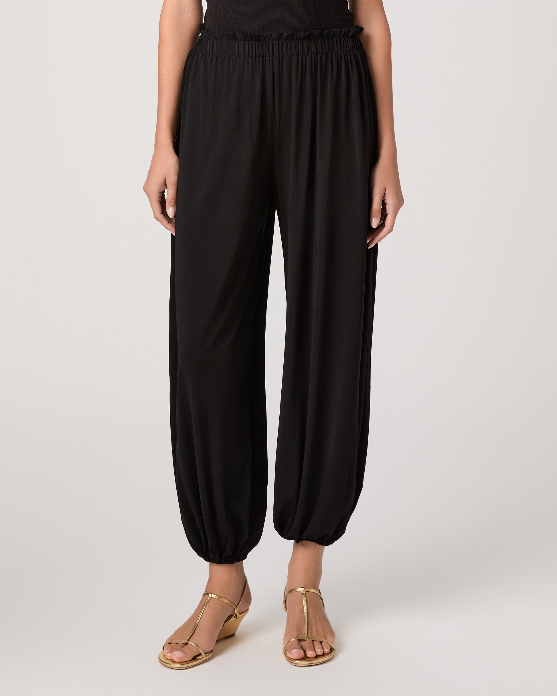 Model wearing a black pant paired with a black off the shoulder top and gold sandals