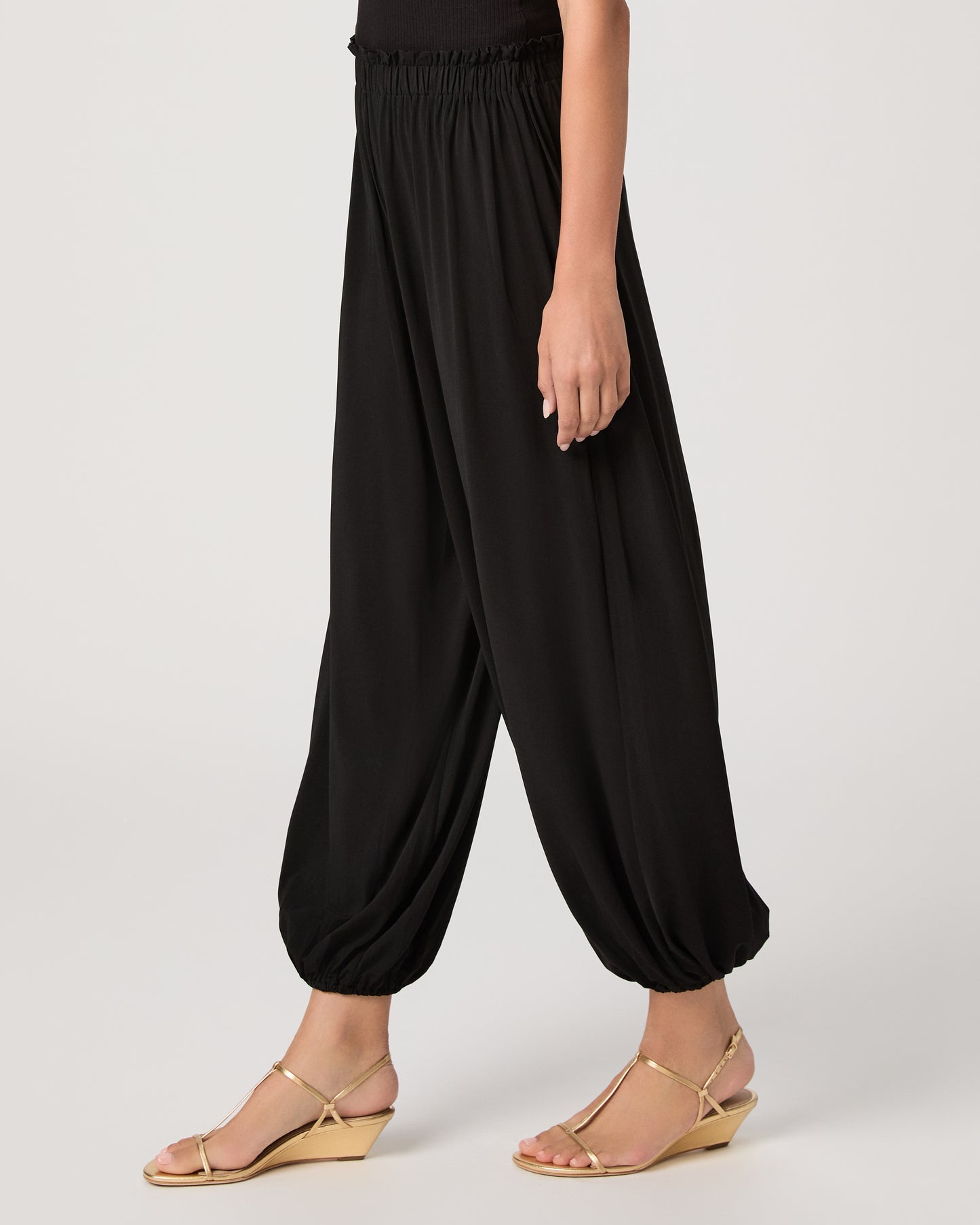 Model wearing a black pant paired with a black off the shoulder top and gold sandals