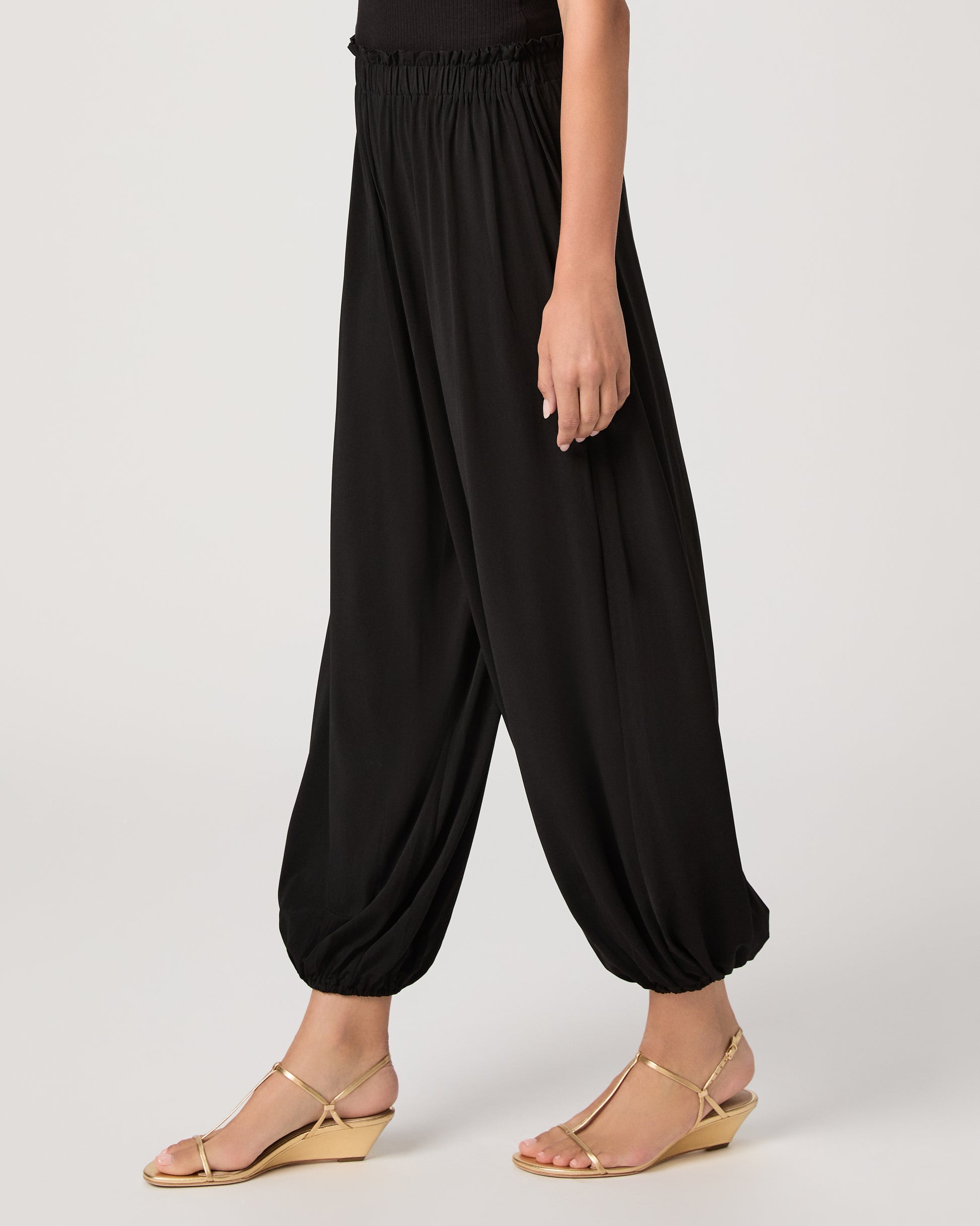 Model wearing a black pant paired with a black off the shoulder top and gold sandals
