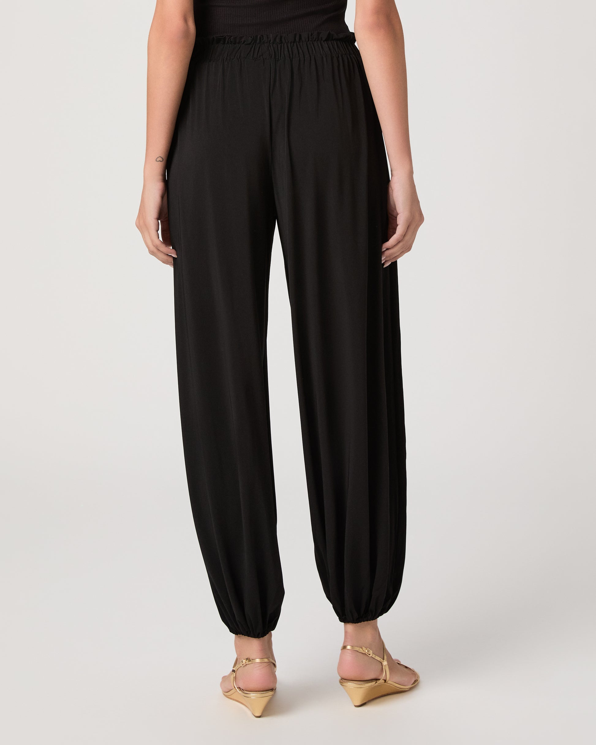 Model wearing a black pant paired with a black off the shoulder top and gold sandals