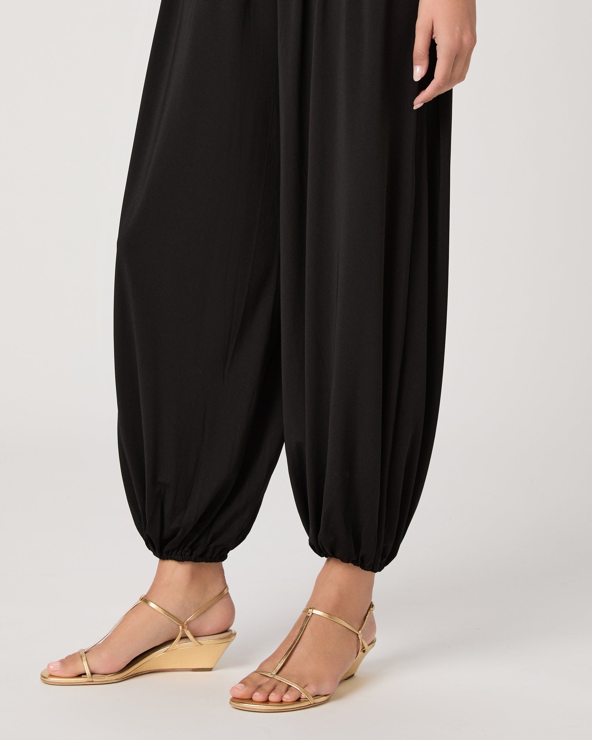 Model wearing a black pant paired with a black off the shoulder top and gold sandals