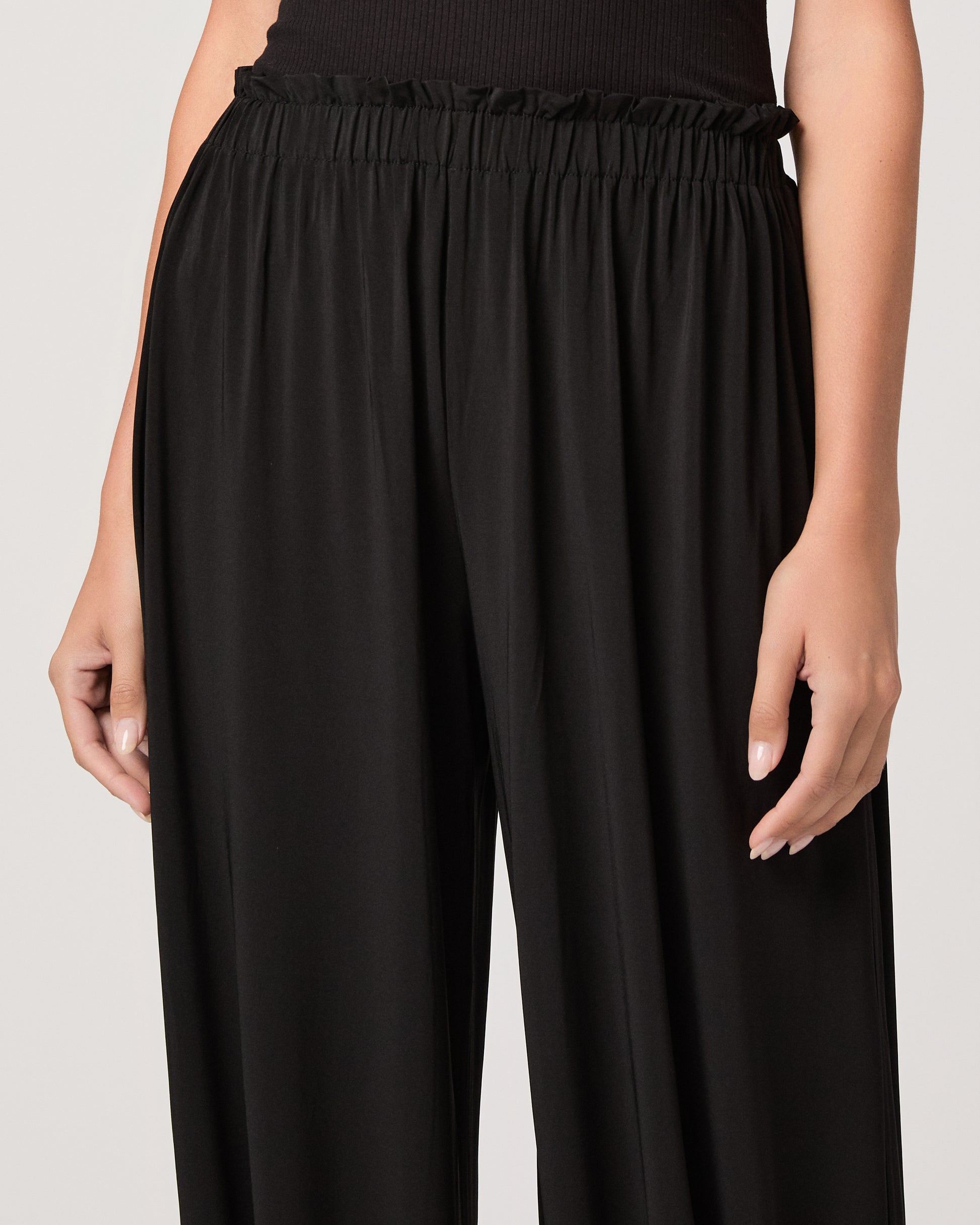 Model wearing a black pant paired with a black off the shoulder top and gold sandals