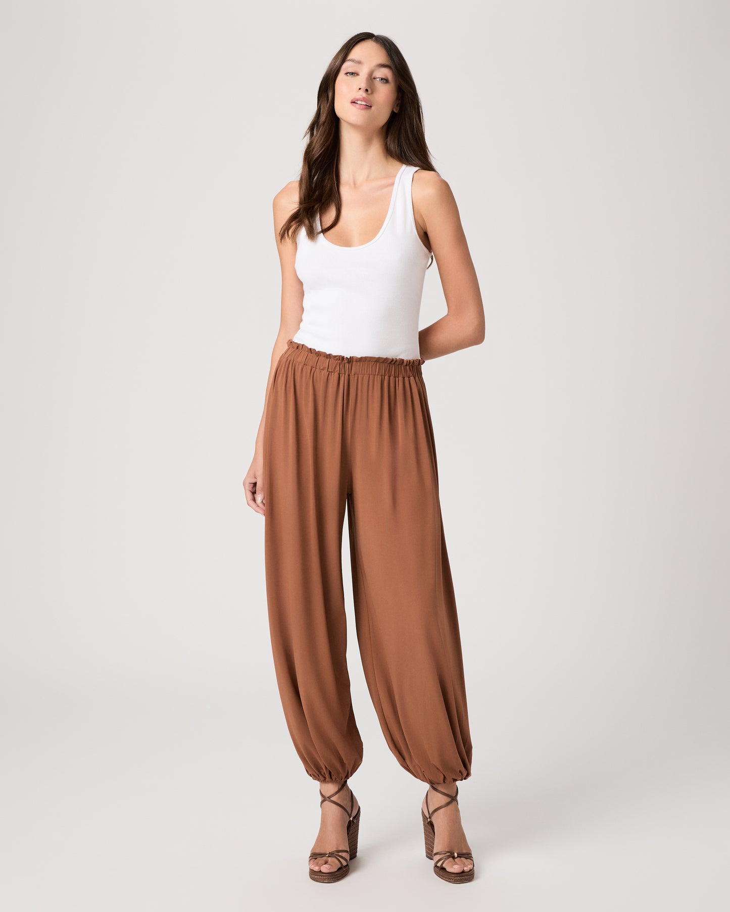 Model wearing an orange pant paired with a white tank top and heeled brown sandals