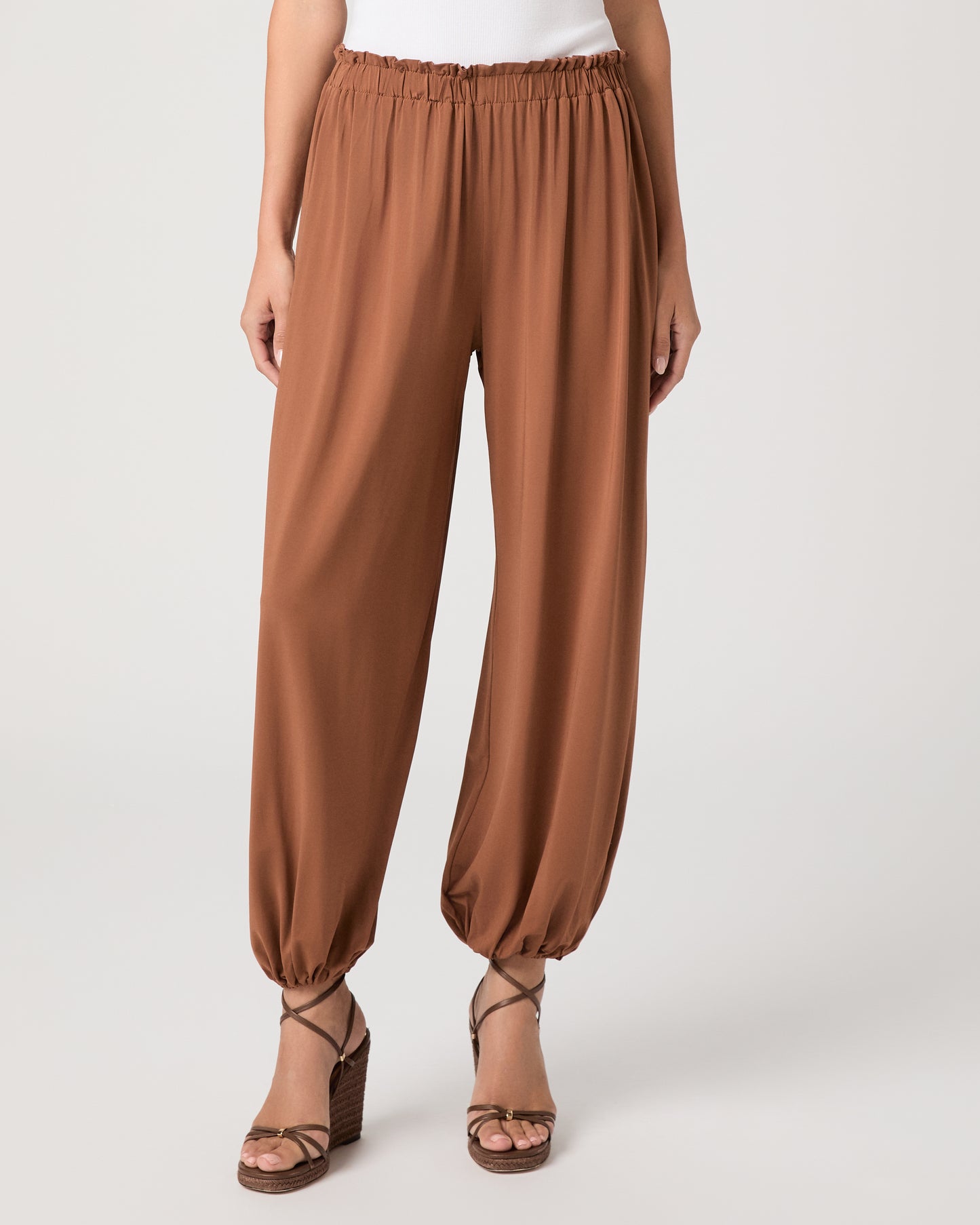 Model wearing an orange pant paired with a white tank top and heeled brown sandals