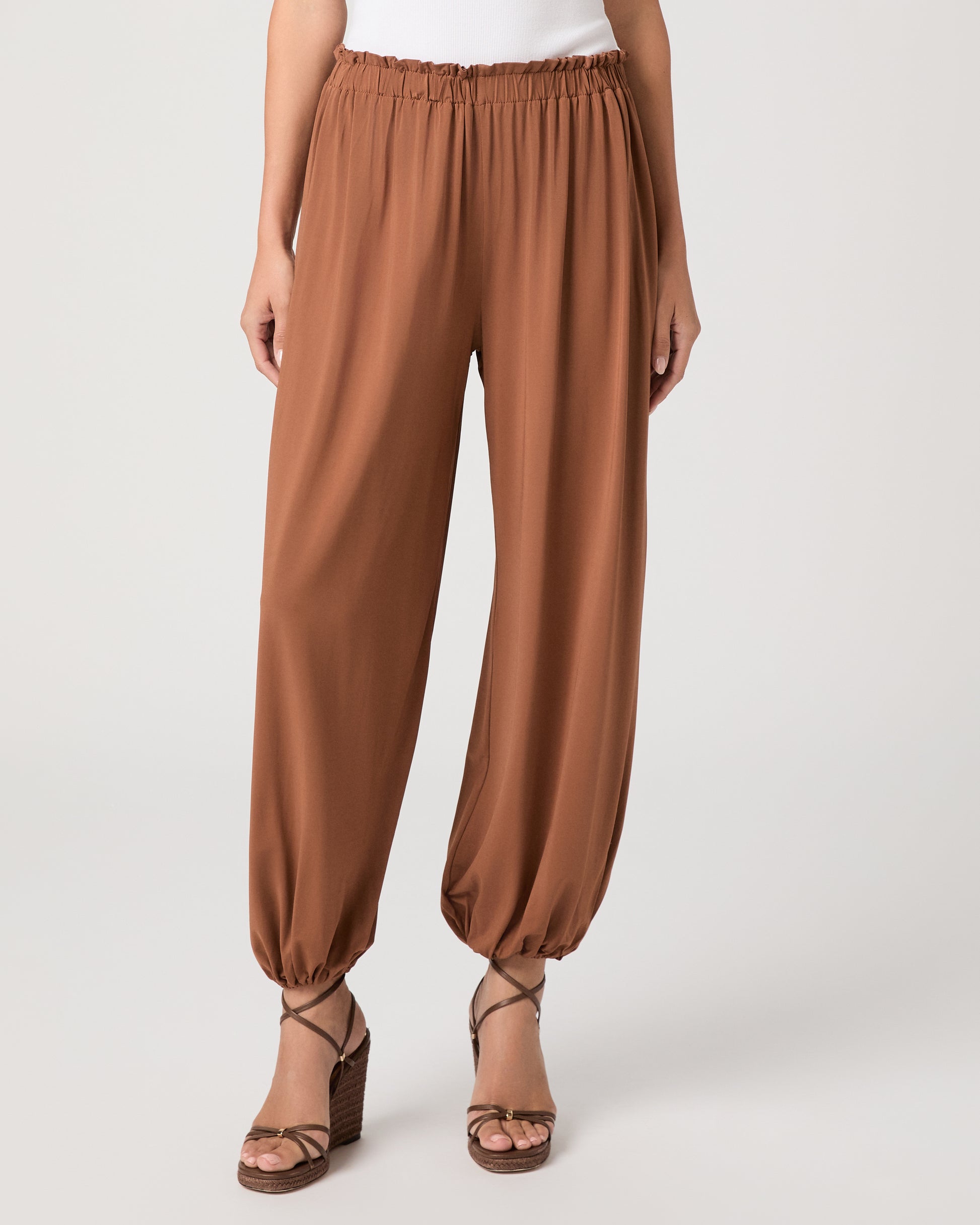 Model wearing an orange pant paired with a white tank top and heeled brown sandals