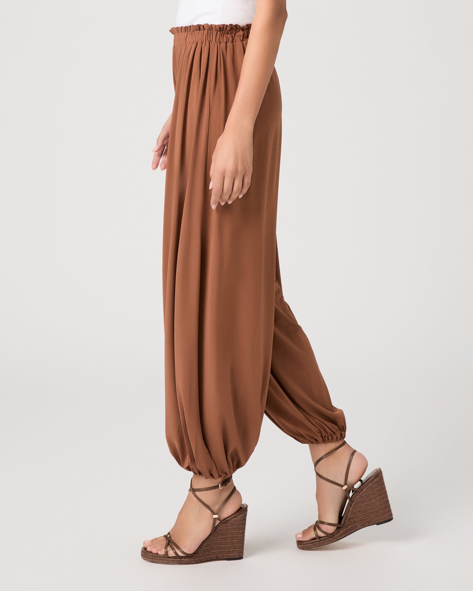Model wearing an orange pant paired with a white tank top and heeled brown sandals