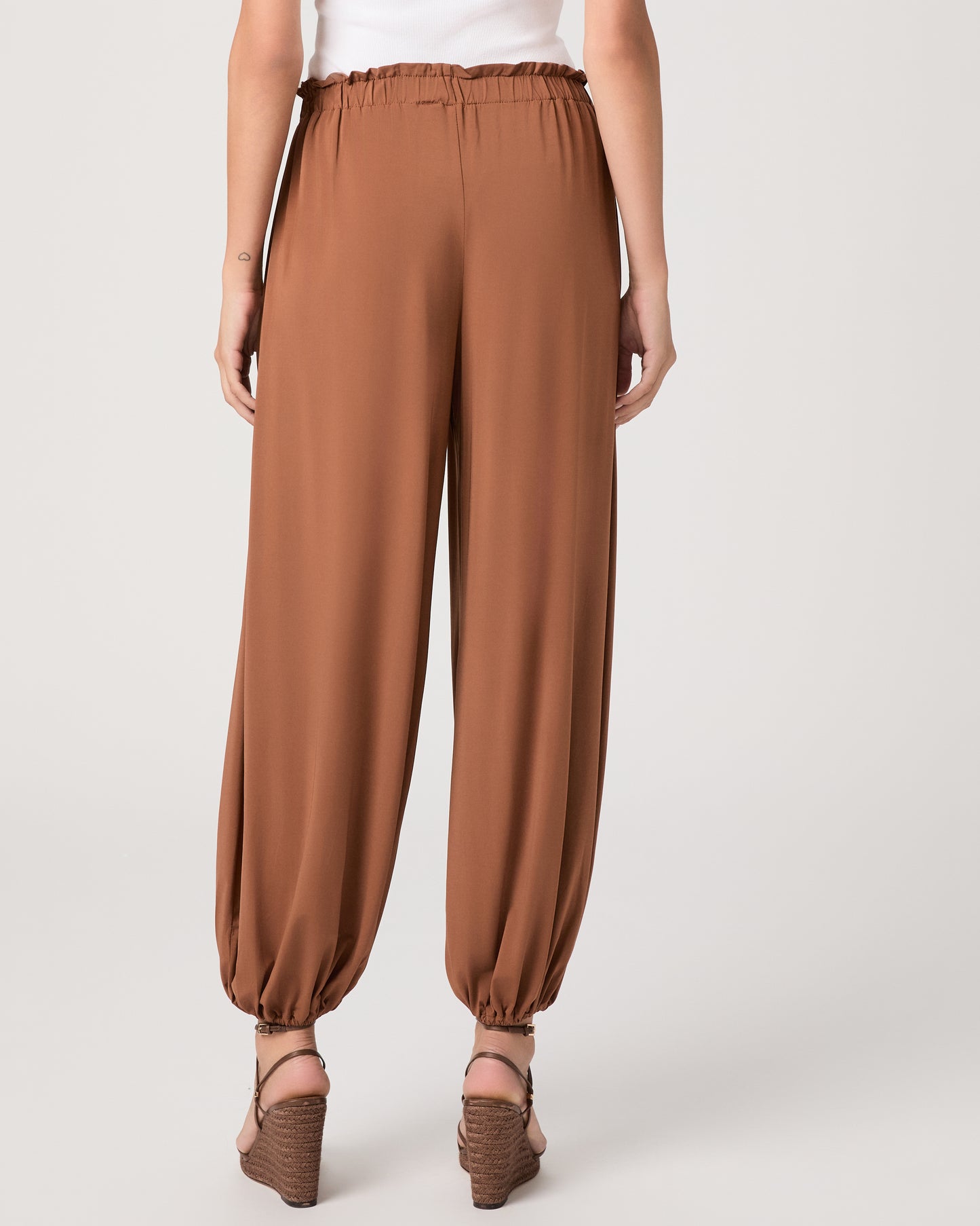 Model wearing an orange pant paired with a white tank top and heeled brown sandals