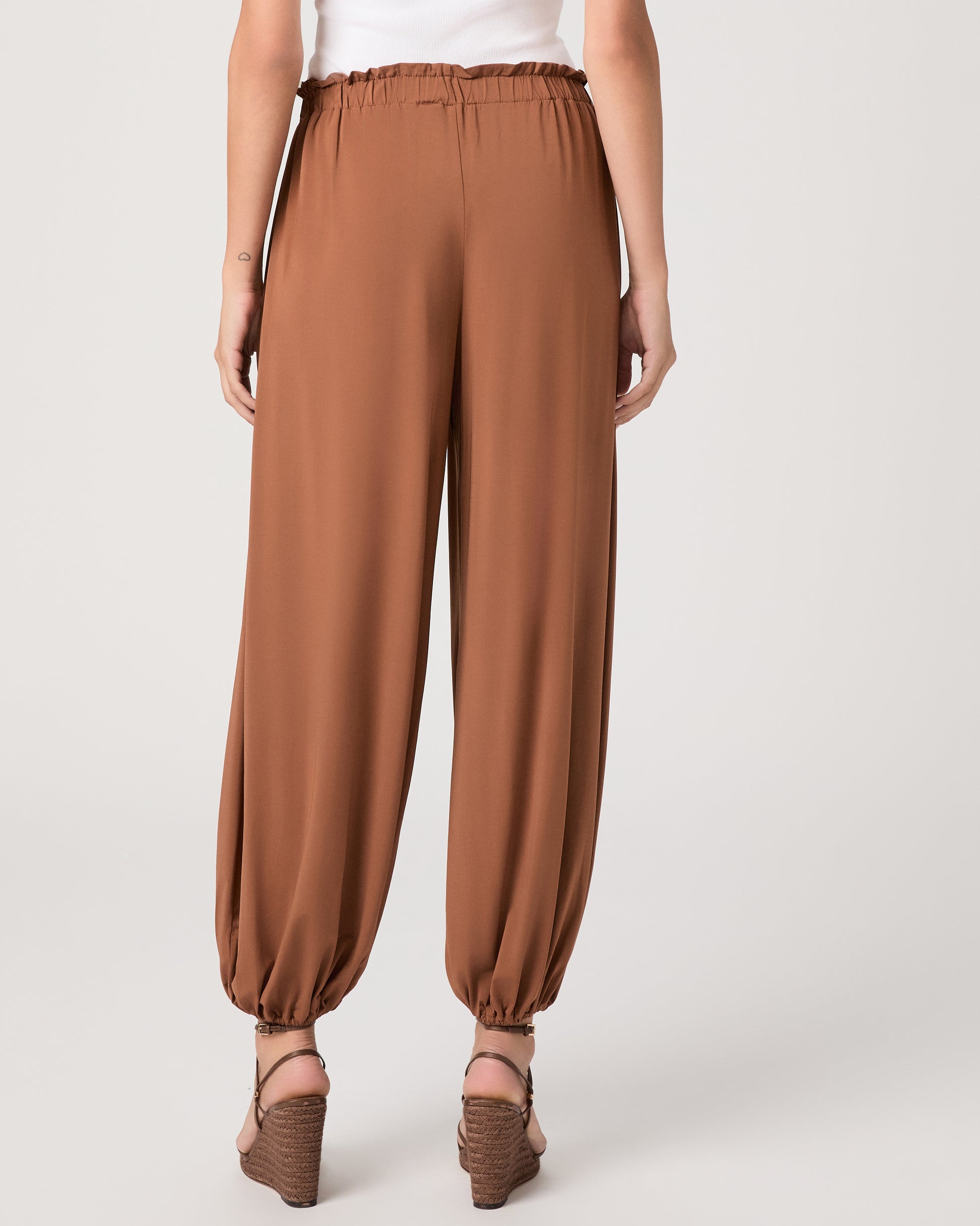 Model wearing an orange pant paired with a white tank top and heeled brown sandals