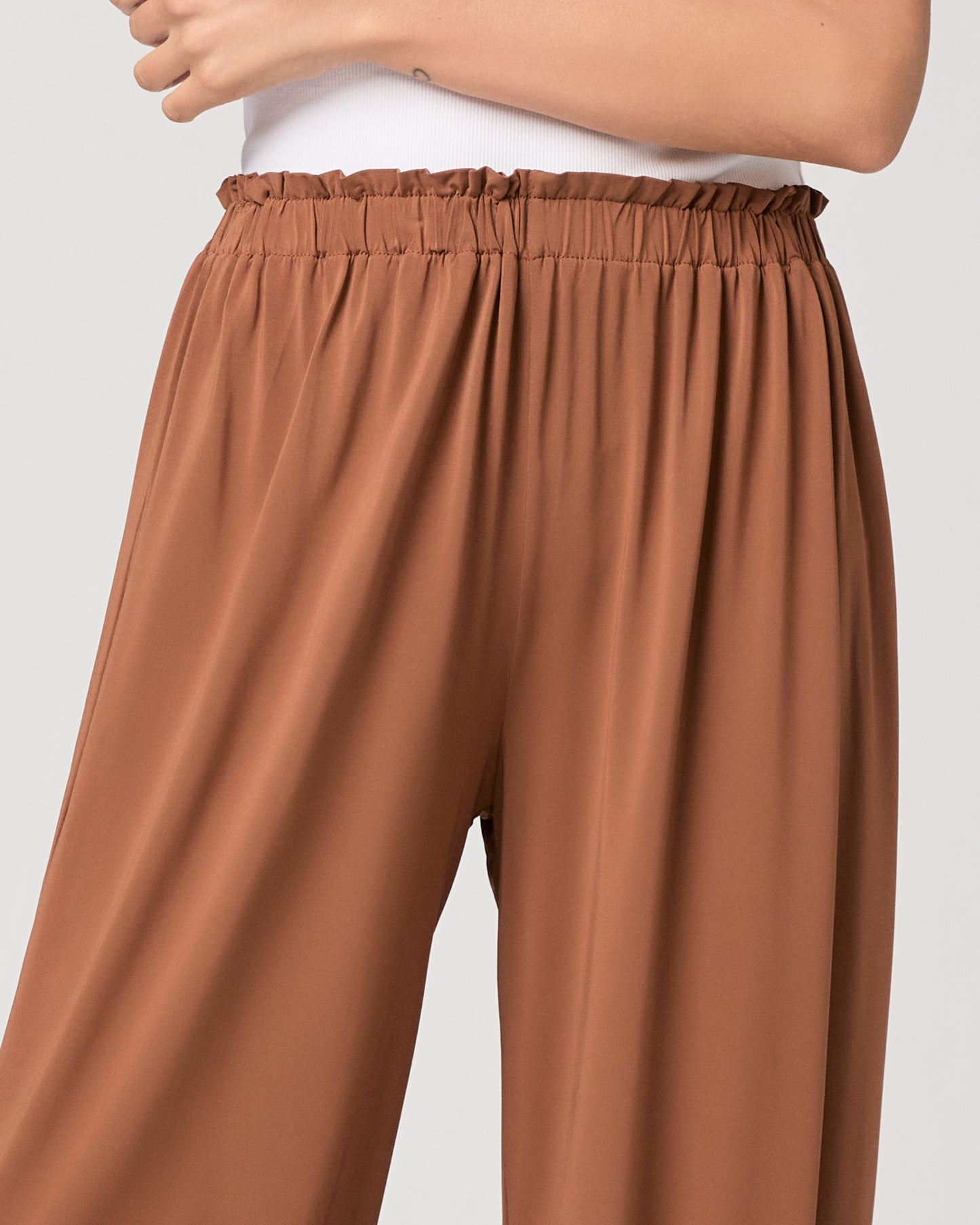 Model wearing an orange pant paired with a white tank top and heeled brown sandals
