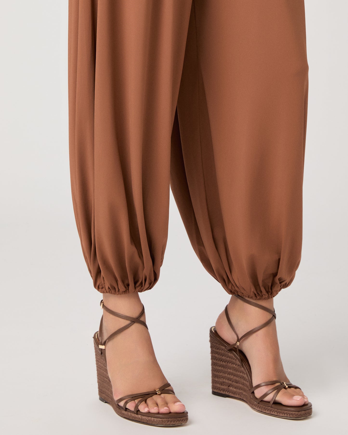 Model wearing an orange pant paired with a white tank top and heeled brown sandals