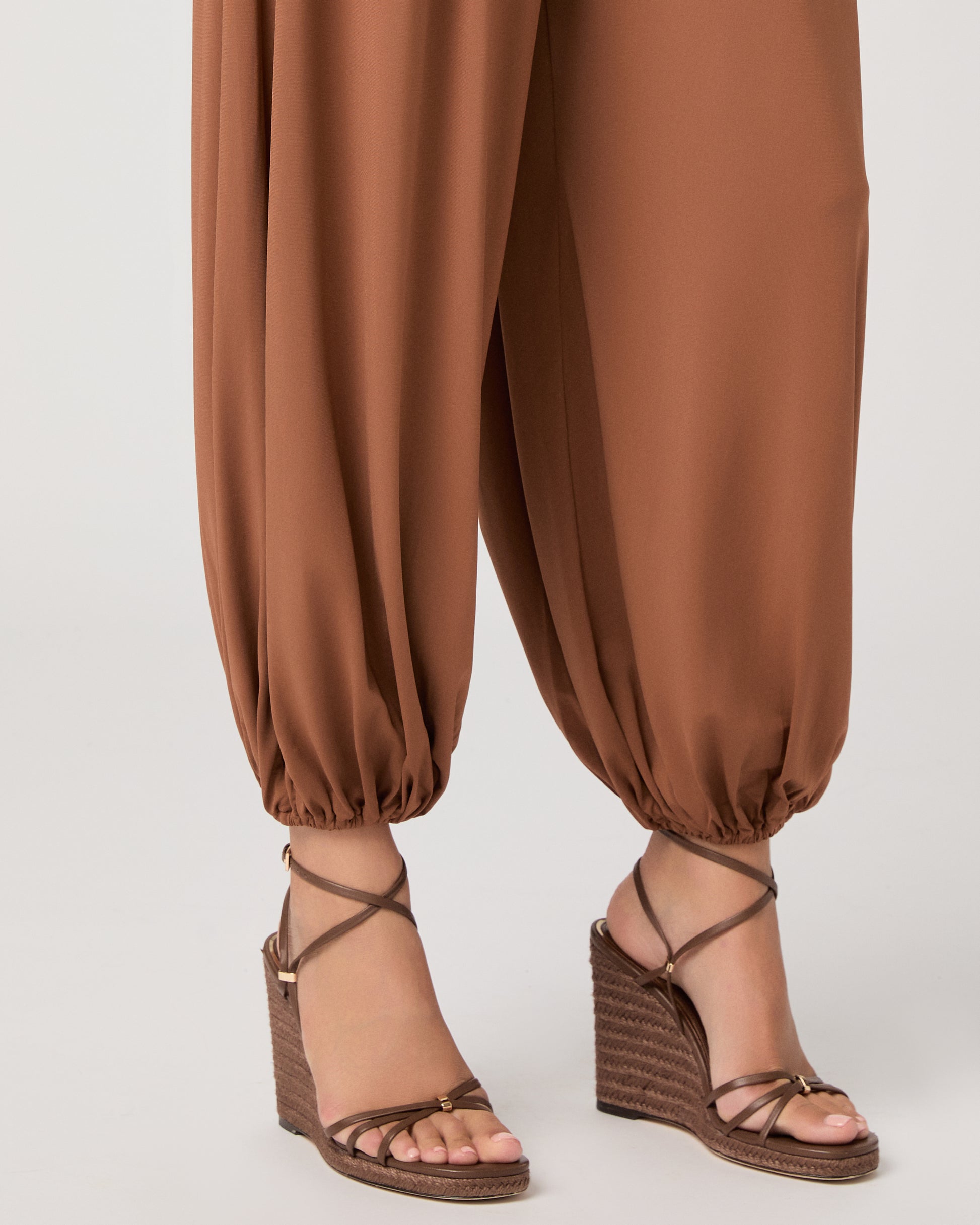 Model wearing an orange pant paired with a white tank top and heeled brown sandals